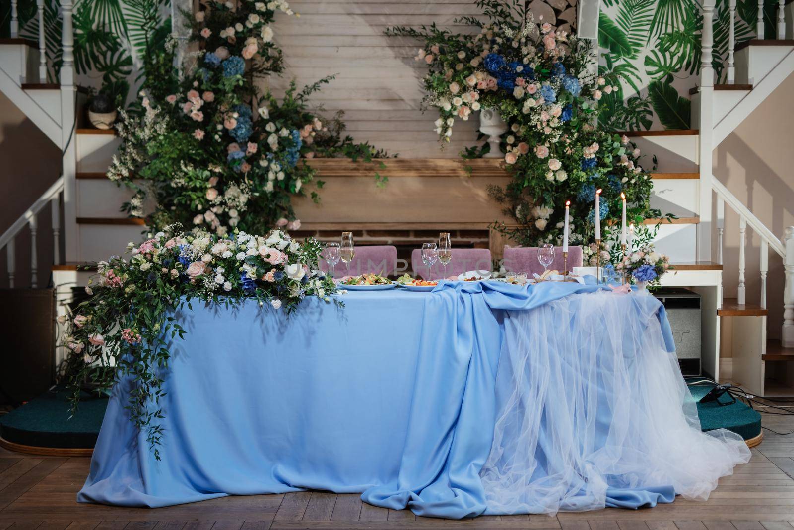 The presidium of the newlyweds in the banquet hall of the restaurant is decorated with candles and green plants, wisteria hangs from the ceiling