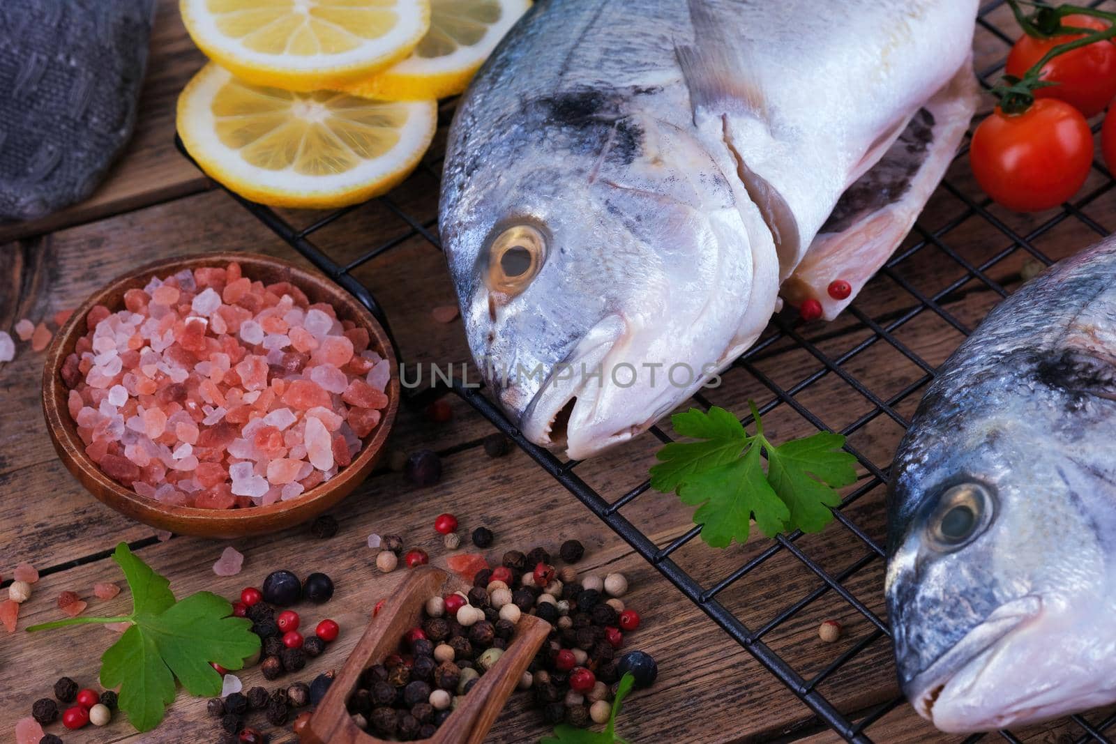 Fresh fish dorado. Raw dorado with salt, pepper, herbs, spices and lemon slices ready to cook on a wooden background. Top view.