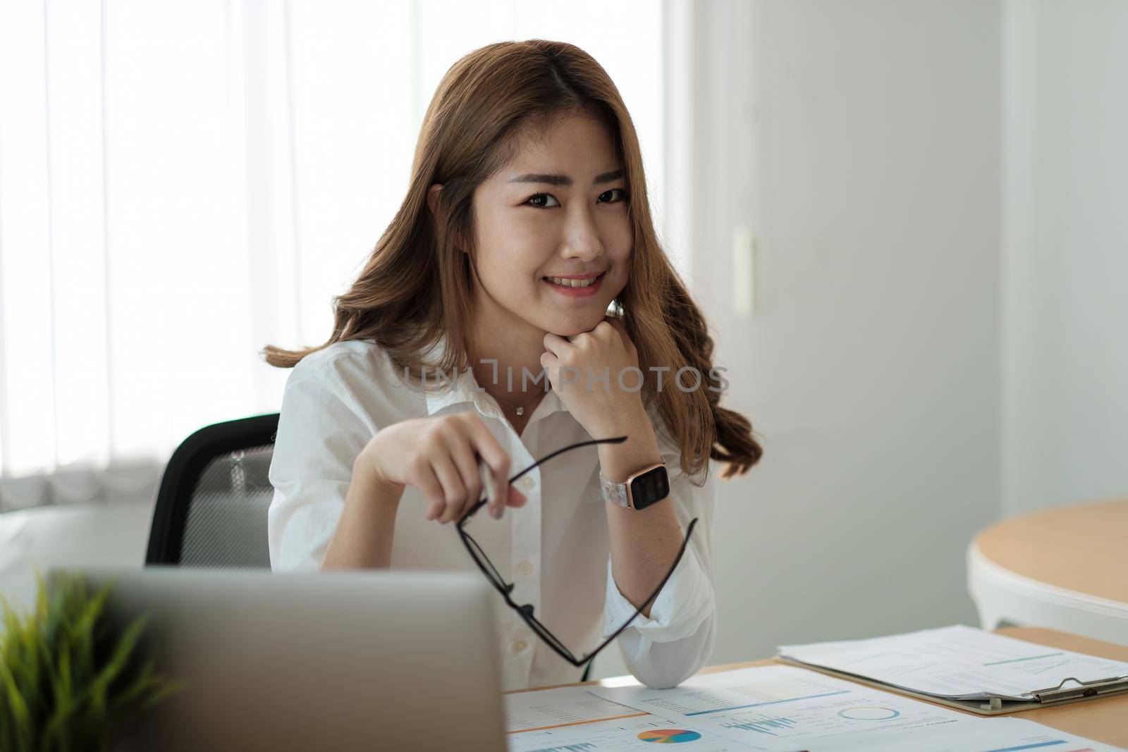 Portrait young beautiful smiling asian business woman holding a glasses and laptop Placed at the wooden table at the office,