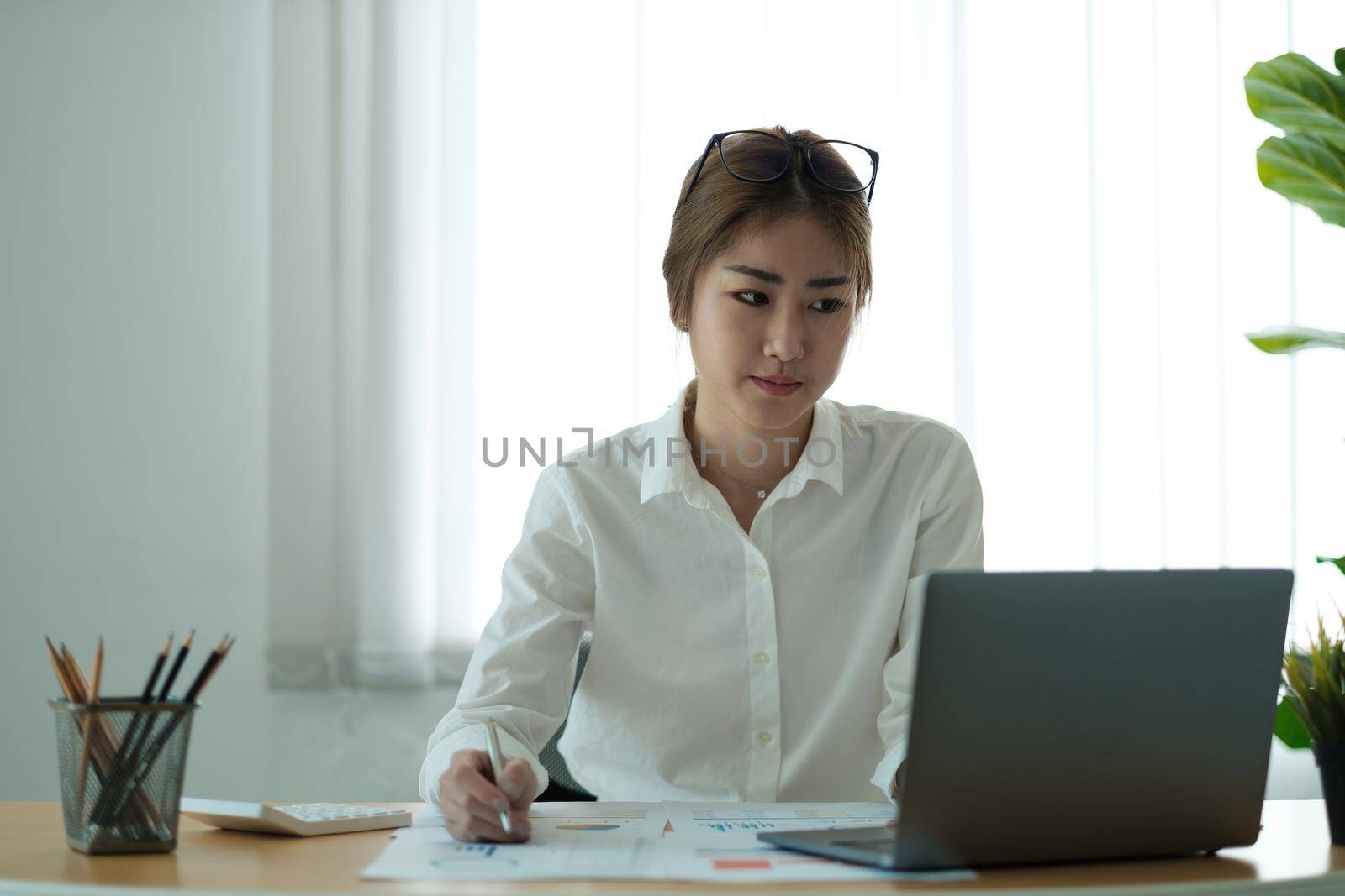Woman accountant use calculator and computer with holding pen on desk in office. finance and accounting concept.