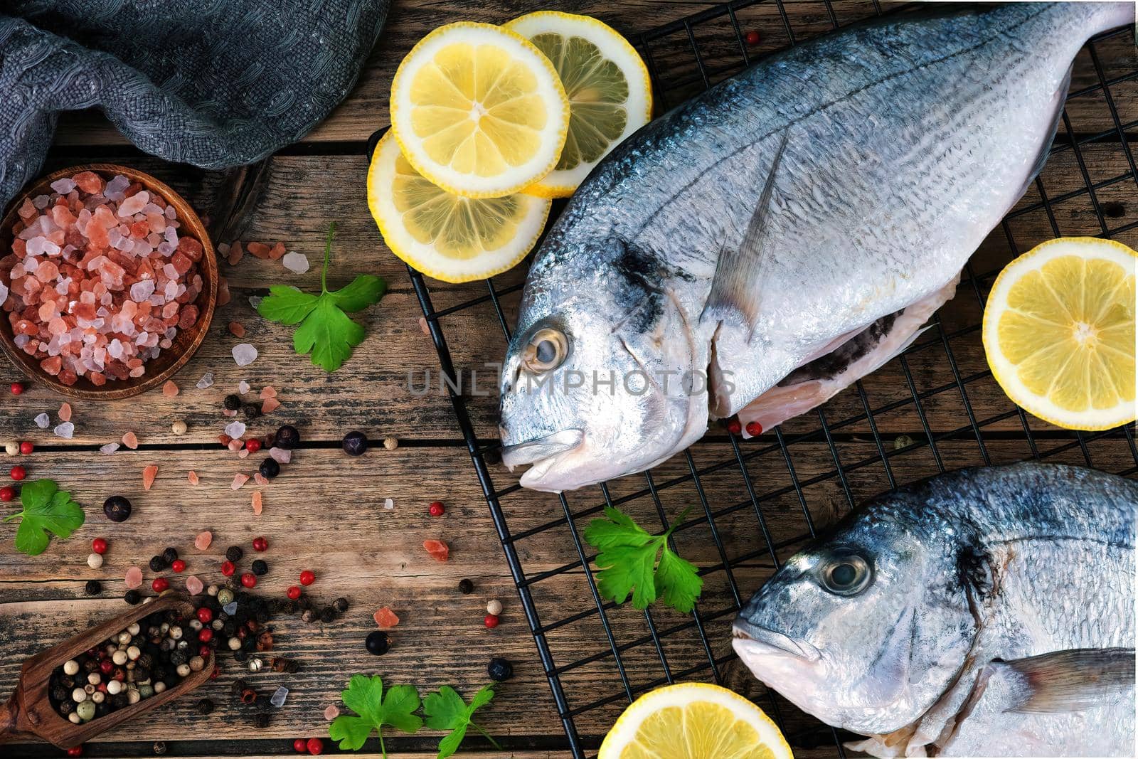 Fresh fish dorado. Raw dorado with salt, pepper, herbs, spices and lemon slices ready to cook on a wooden background. Top view.