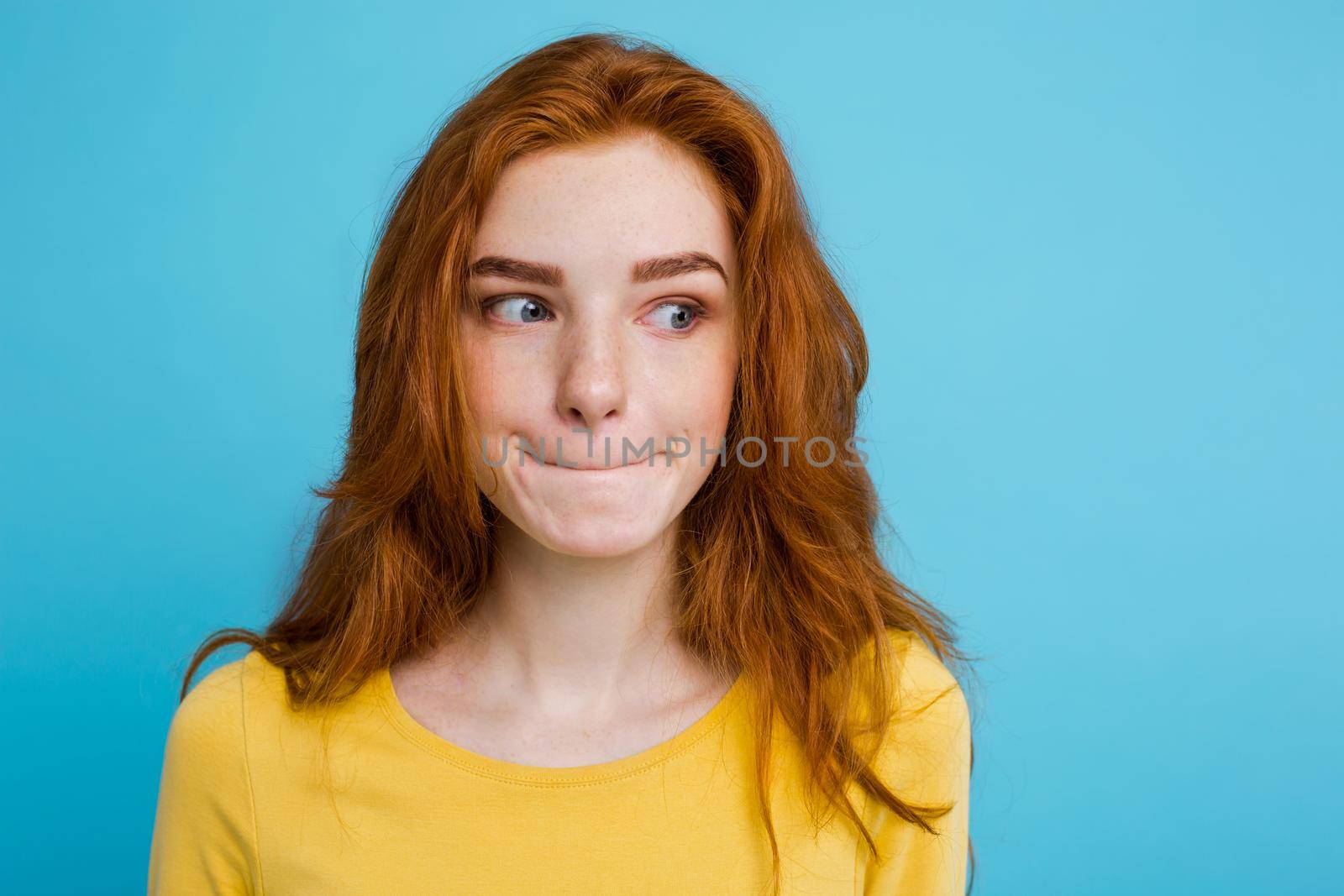 Headshot Portrait of happy ginger red hair girl with freckles smiling looking at camera. Pastel blue background. Copy Space by Benzoix