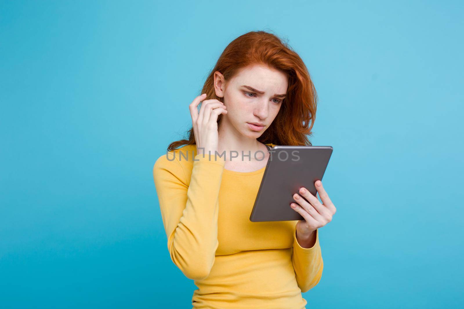 Close up Portrait young beautiful attractive tender ginger redhair girl happy smiling on digital table with wining something. Blue Pastel Background. Copy space.