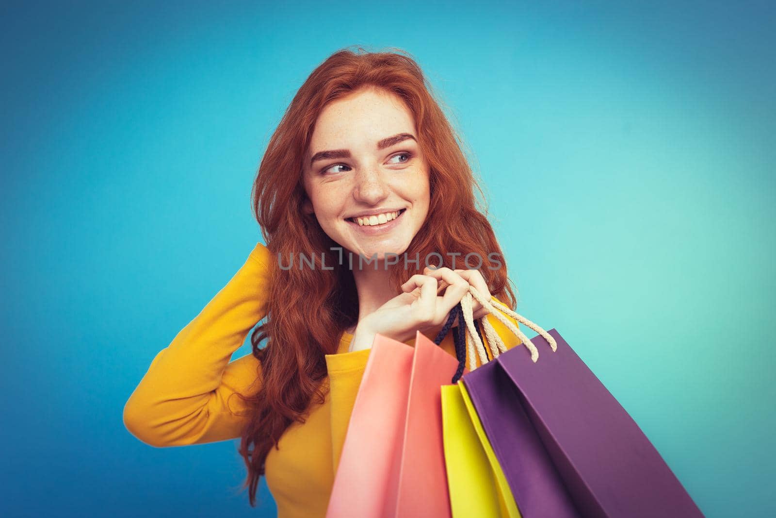 Shopping Concept - Close up Portrait young beautiful attractive redhair girl smiling looking at camera with shopping bag. Blue Pastel Background. Copy space by Benzoix