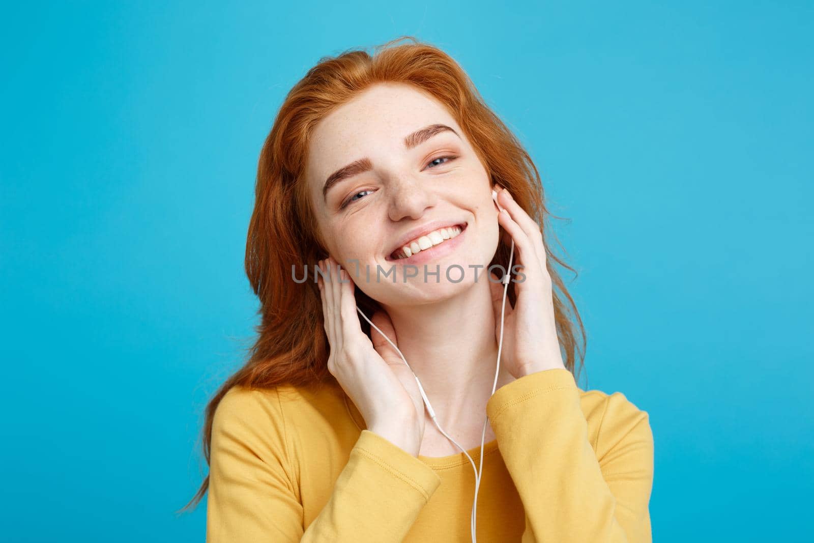 Lifestyle concept - Portrait of cheerful happy ginger red hair girl enjoy listening to music with headphones joyful smiling to camera. Isolated on Blue Pastel Background. Copy space. by Benzoix