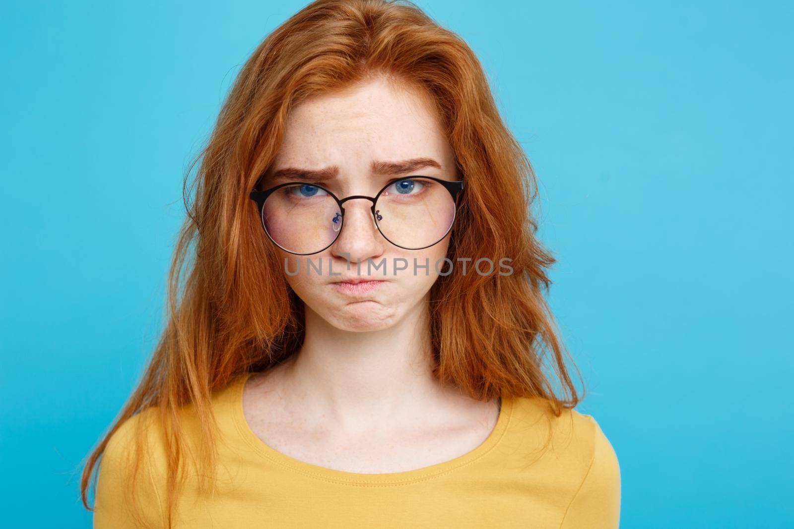 Headshot Portrait of happy ginger red hair girl with freckles smiling looking at camera. Pastel blue background. Copy Space.