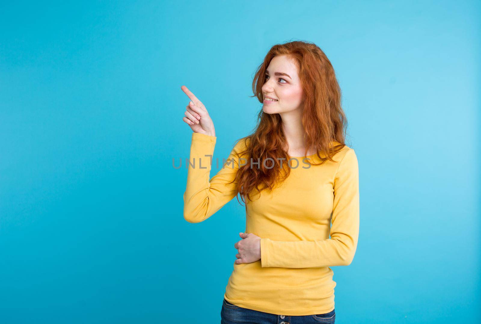 Close up Portrait young beautiful attractive redhair girl happy with something and pointing finger. Blue Pastel Background. Copy space by Benzoix