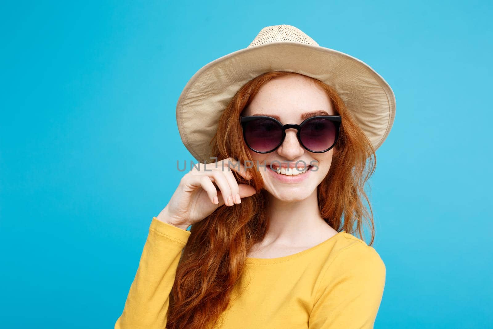 Travel concept - Close up Portrait young beautiful attractive ginger red hair girl with trendy hat and sunglass smiling. Blue Pastel Background. Copy space.