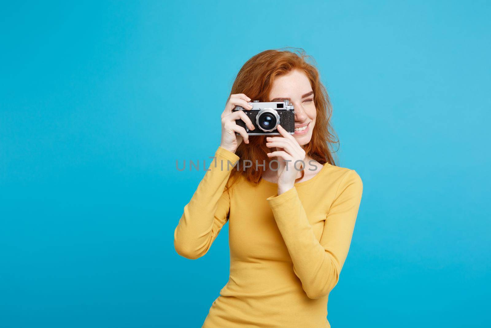 Travel and People Concept - Headshot Portrait of happy ginger red hair girl ready to travel with vintage camera in happy expression. Pastel blue background. Copy Space. by Benzoix