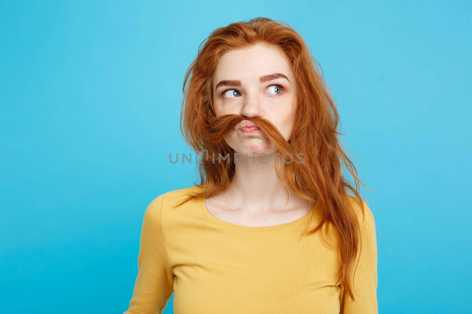 Headshot Portrait of happy ginger red hair girl imitating to be man with hair fake mustache. Pastel blue background. Copy Space. by Benzoix