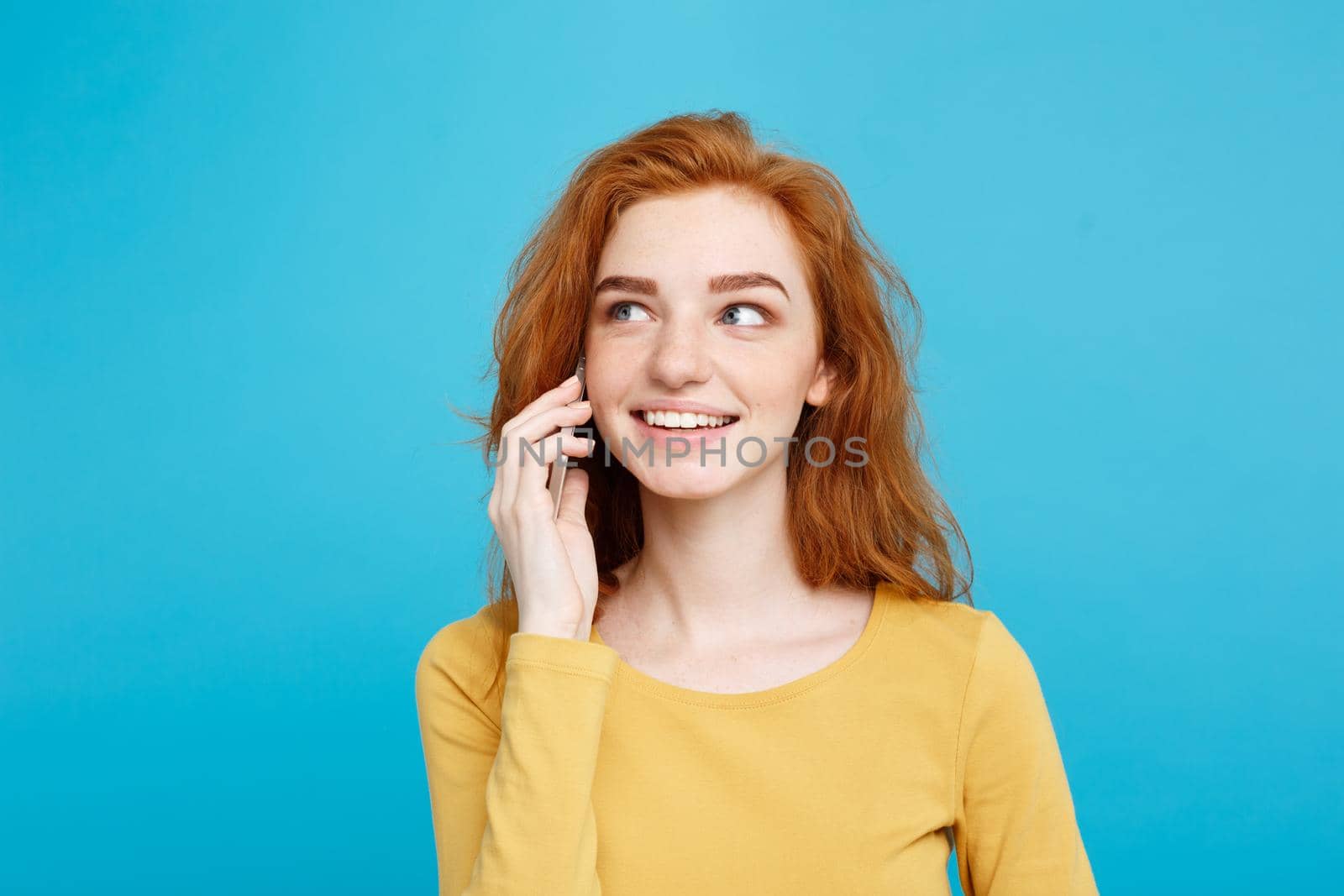 Lifestyle and Technology concept - Portrait of cheerful happy ginger red hair girl with joyful and exciting talking with friend by mobile phone. Isolated on Blue Pastel Background. Copy space. by Benzoix