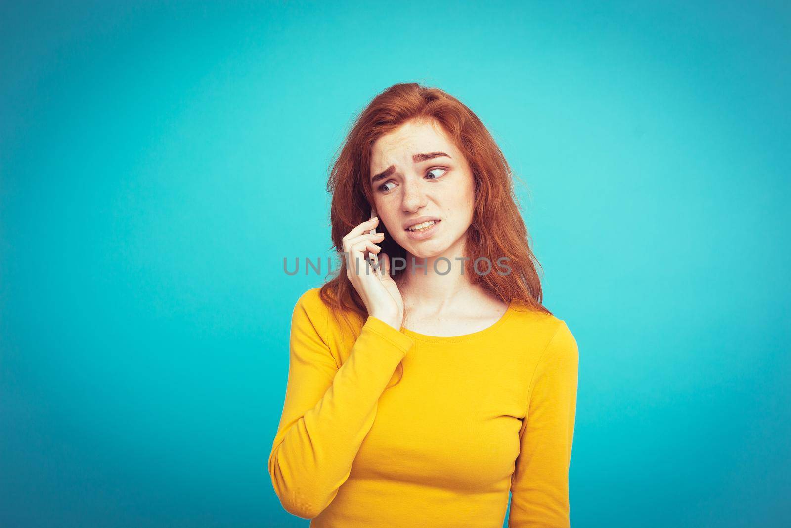 Lifestyle concept - Portrait of ginger red hair girl with shocking and stressful expression while talking with friend by mobile phone. Isolated on Blue Pastel Background. Copy space by Benzoix