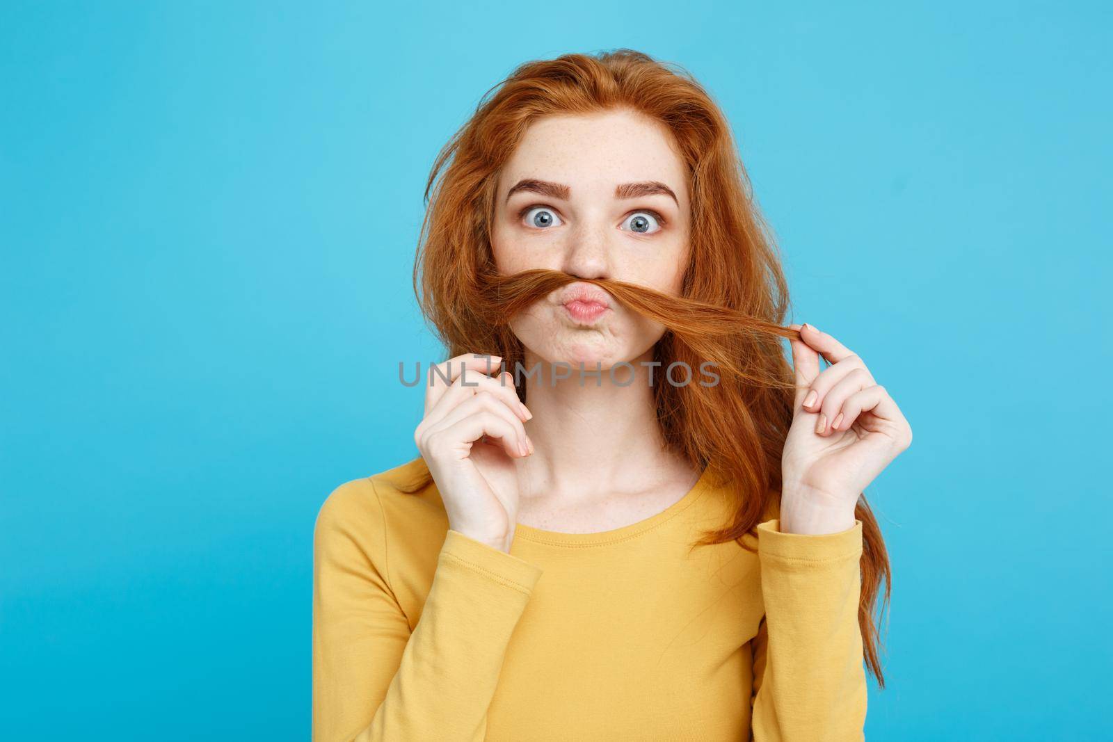 Headshot Portrait of happy ginger red hair girl imitating to be man with hair fake mustache.Pastel blue background. Copy Space.