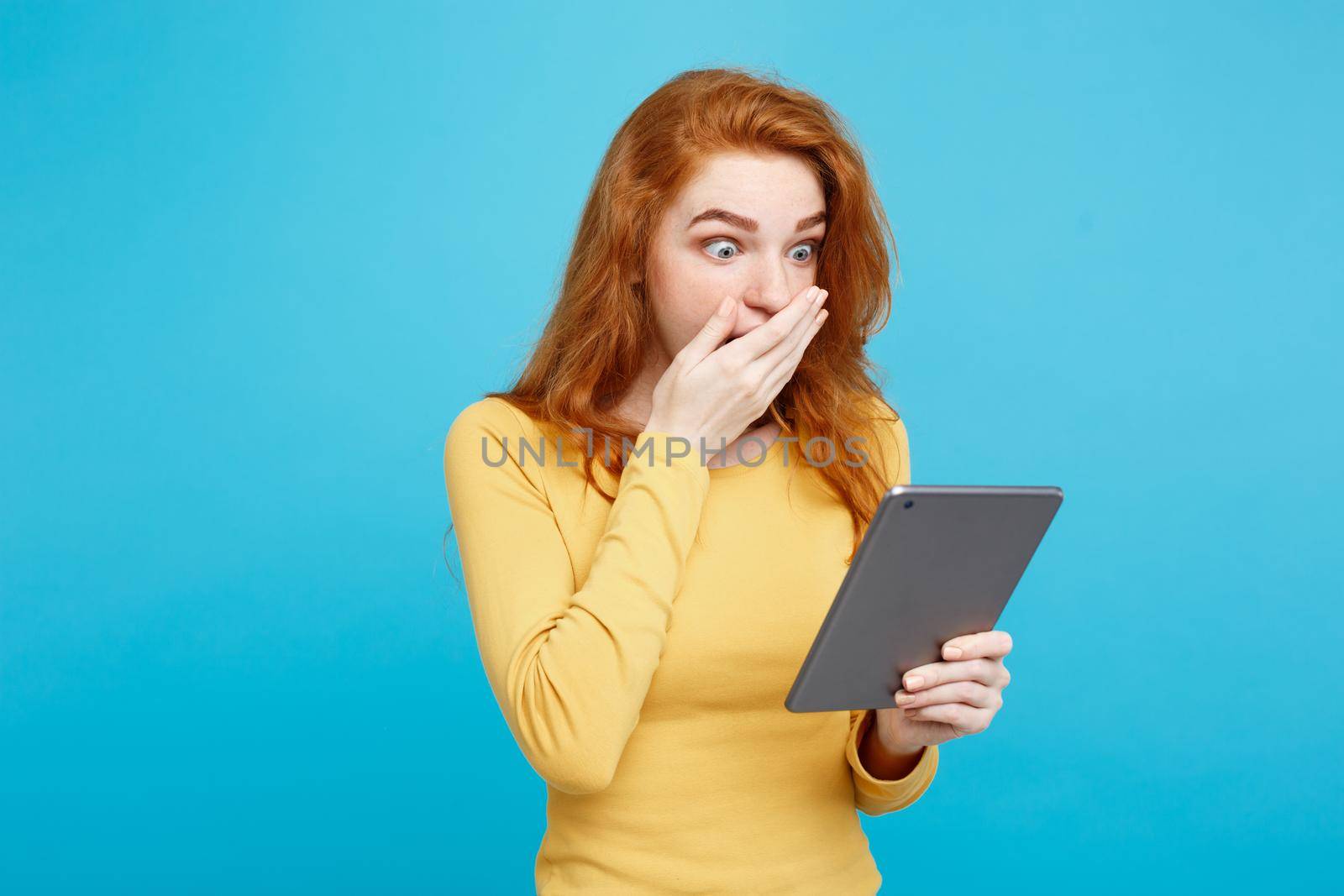 People and Technology Concept - Close up Portrait young beautiful attractive tender ginger redhair girl happy smiling on digital table with wining something. Blue Pastel Background. Copy space. by Benzoix