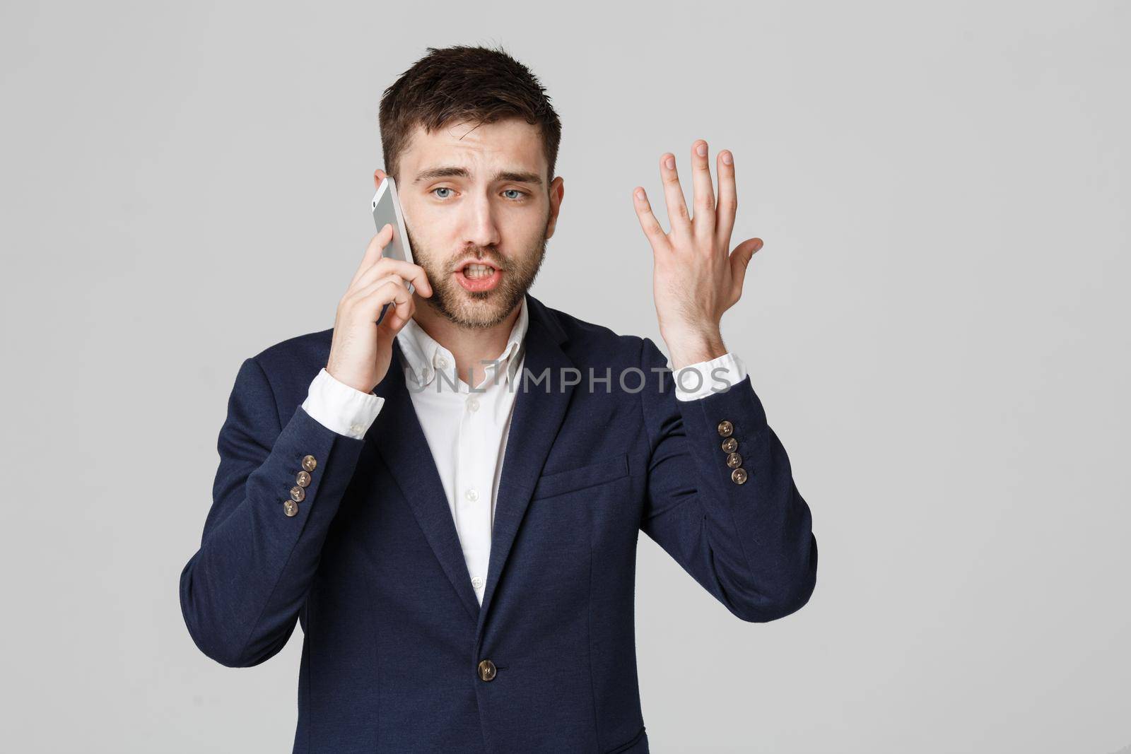 Business Concept - Portrait young handsome angry business man in suit talking on phone looking at camera. White background.