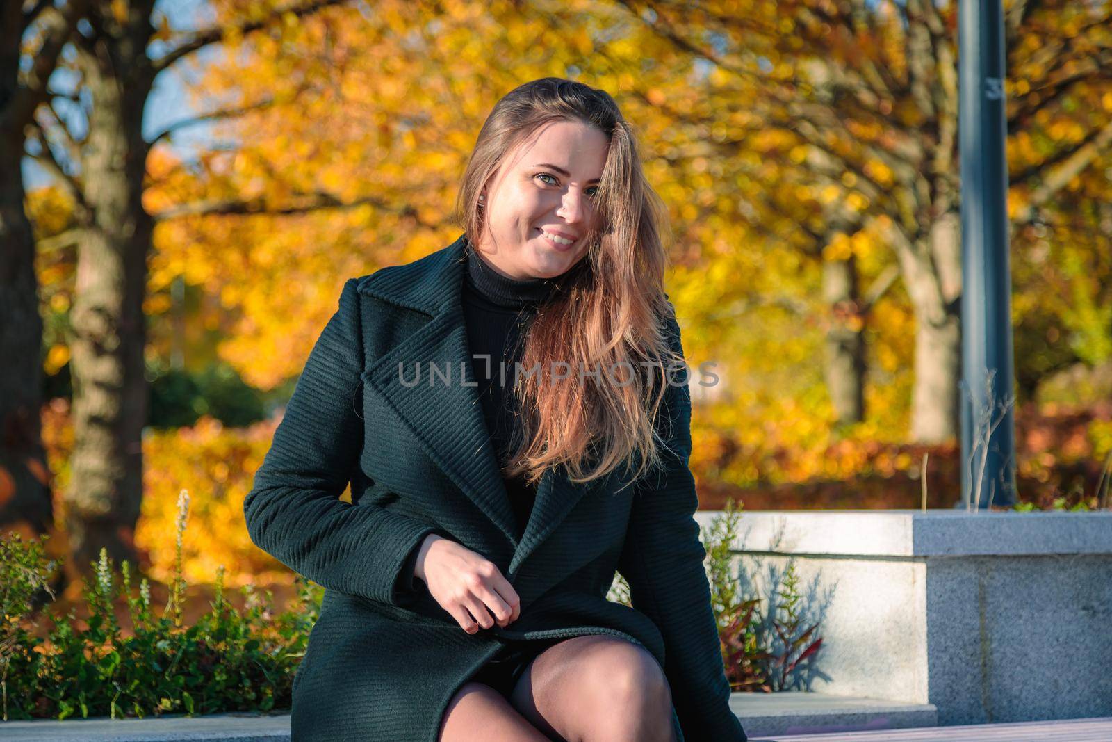 A woman with long hair sits on a bench in an autumn park and laughs. Autumn season.