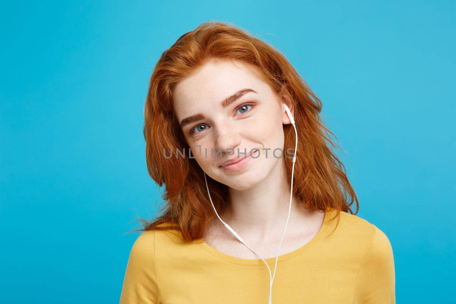 Lifestyle concept - Portrait of cheerful happy ginger red hair girl enjoy listening to music with headphones joyful smiling to camera. Isolated on Blue Pastel Background. Copy space. by Benzoix