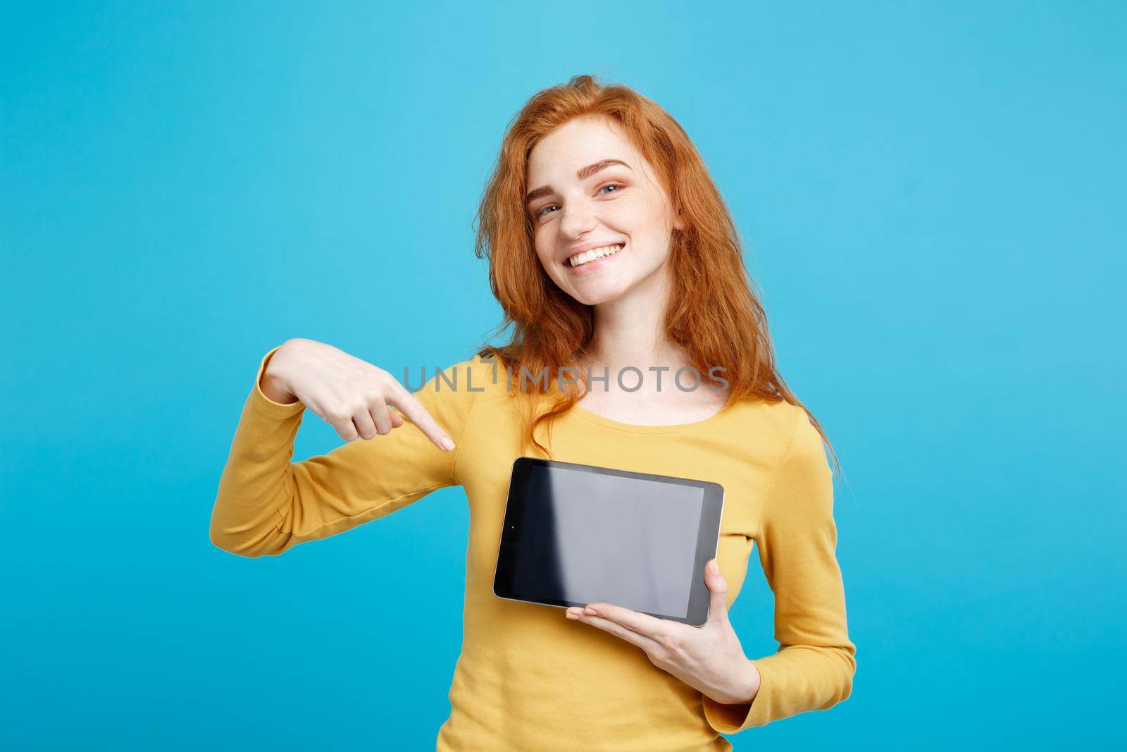 Close up Portrait young beautiful attractive redhair girl smiling showing digital tablet screen on black. Blue Pastel Background. Copy space.