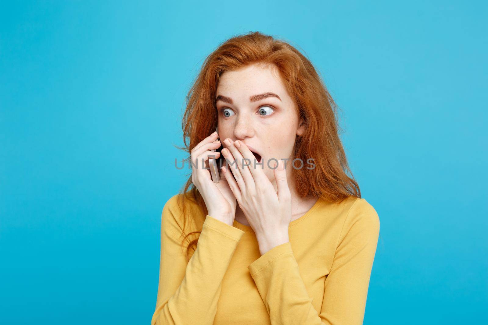 Lifestyle concept - Portrait of ginger red hair girl with shocking and stressful expression while talking with friend by mobile phone. Isolated on Blue Pastel Background. Copy space. by Benzoix