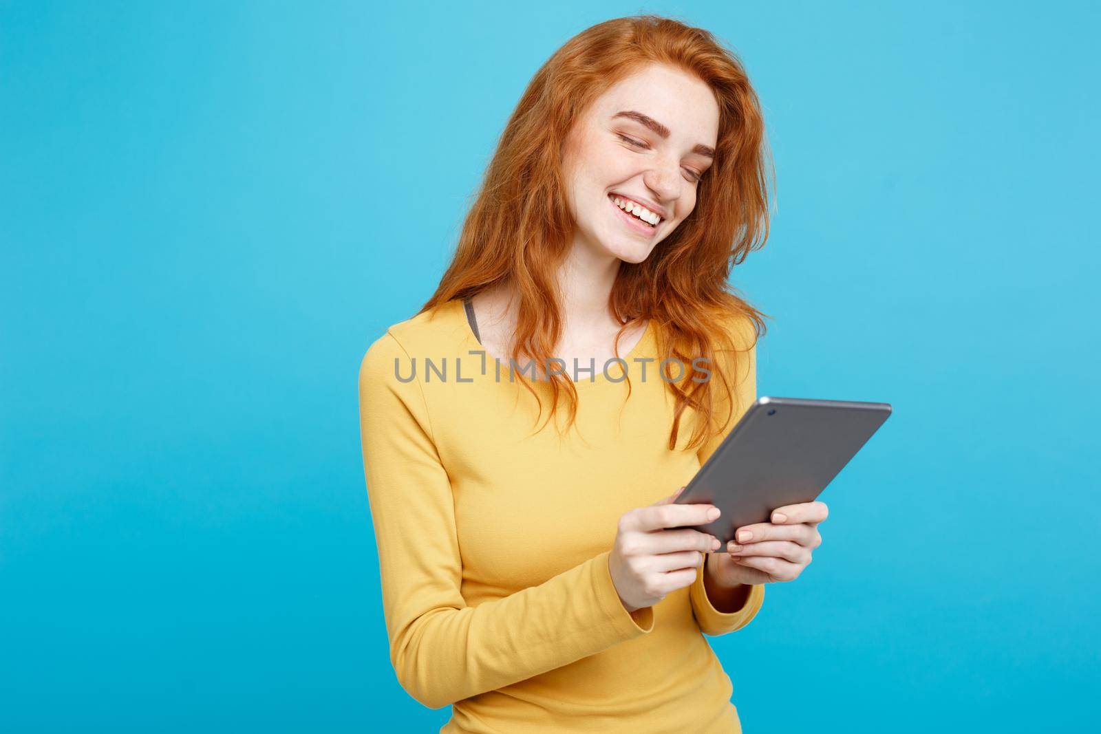 People and Technology Concept - Close up Portrait young beautiful attractive tender ginger redhair girl happy smiling on digital table with wining something. Blue Pastel Background. Copy space. by Benzoix