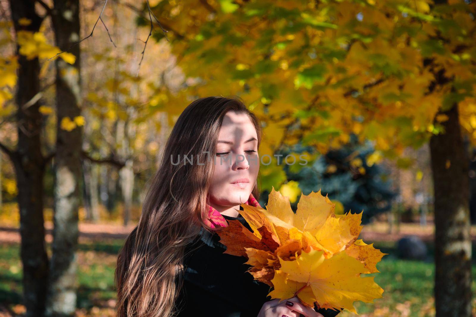 A woman with long hair looks at yellow leaves in an autumn park. Autumn season.