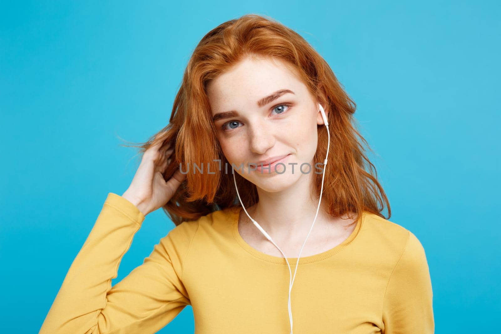 Lifestyle concept - Portrait of cheerful happy ginger red hair girl enjoy listening to music with headphones joyful smiling to camera. Isolated on Blue Pastel Background. Copy space. by Benzoix