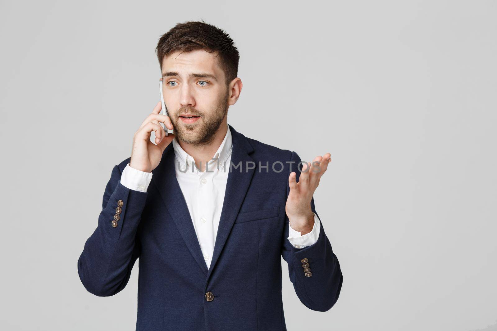 Business Concept - Portrait young handsome angry business man in suit talking on phone looking at camera. White background.