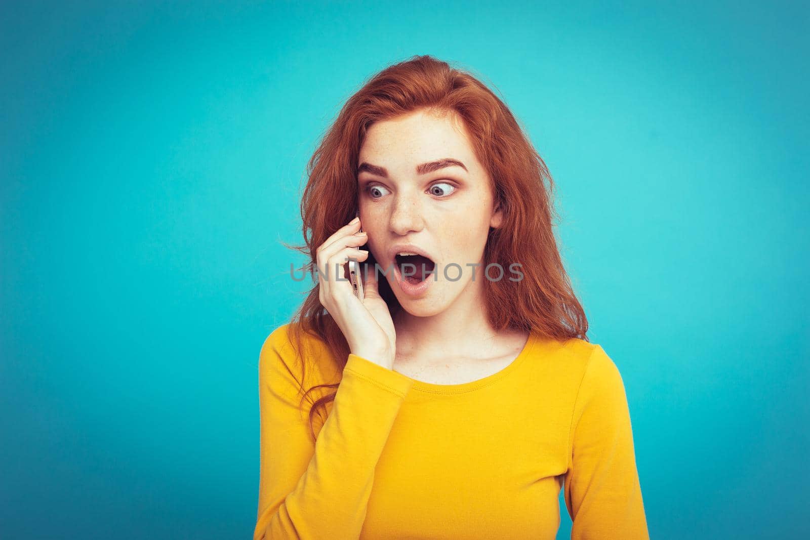 Lifestyle and Technology concept - Portrait of cheerful happy ginger red hair girl with joyful and exciting talking with friend by mobile phone. Isolated on Blue Pastel Background. Copy space.