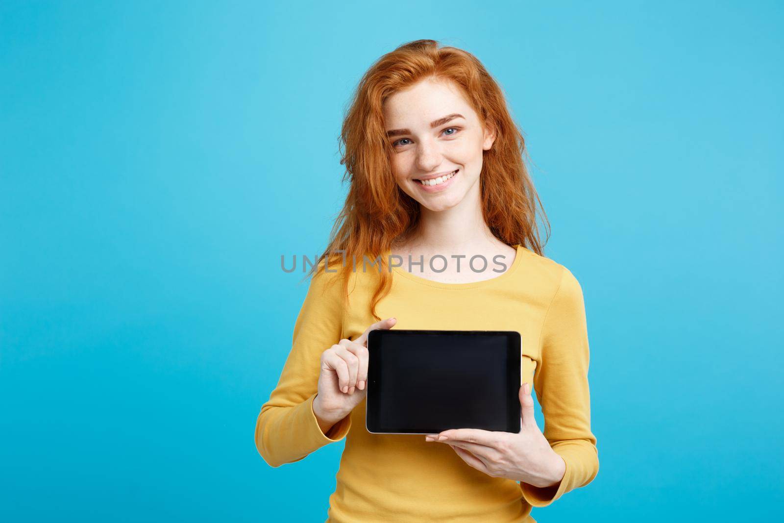Business Concept - Close up Portrait young beautiful attractive redhair girl smiling showing digital tablet screen on black. Blue Pastel Background.