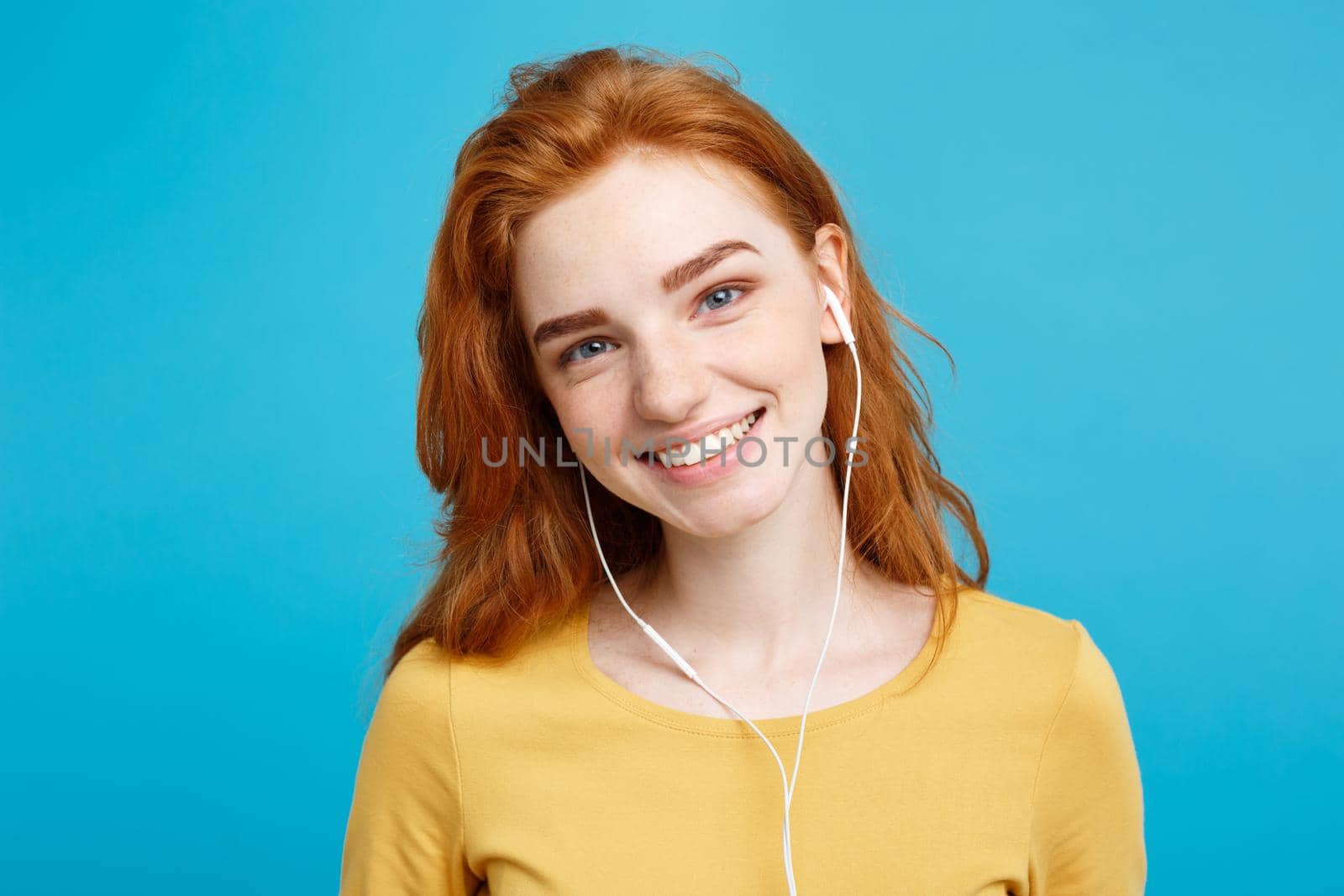 Lifestyle concept - Portrait of cheerful happy ginger red hair girl enjoy listening to music with headphones joyful smiling to camera. Isolated on Blue Pastel Background. Copy space.