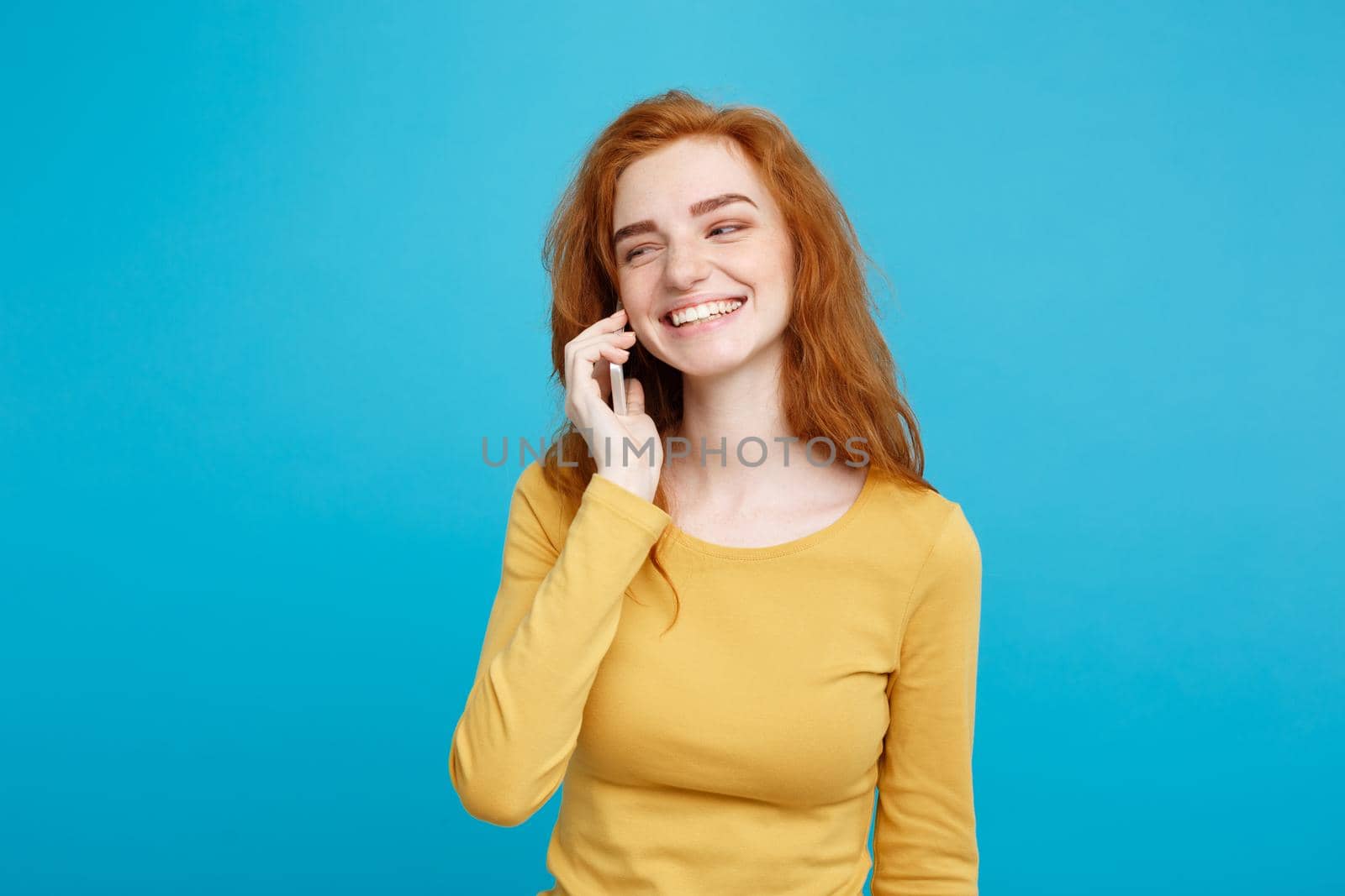Lifestyle and Technology concept - Portrait of cheerful happy ginger red hair girl with joyful and exciting talking with friend by mobile phone. Isolated on Blue Pastel Background. Copy space. by Benzoix