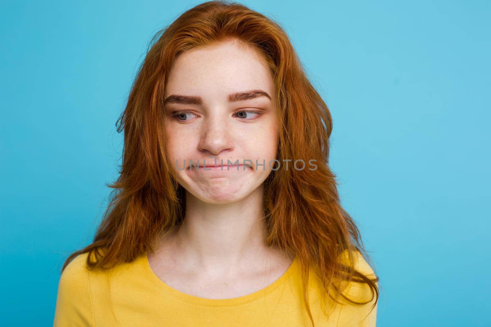 Headshot Portrait of tender redhead teenage girl with serious expression looking at camera. Caucasian woman model with ginger hair posing indoors.Pastel blue background. Copy Space by Benzoix