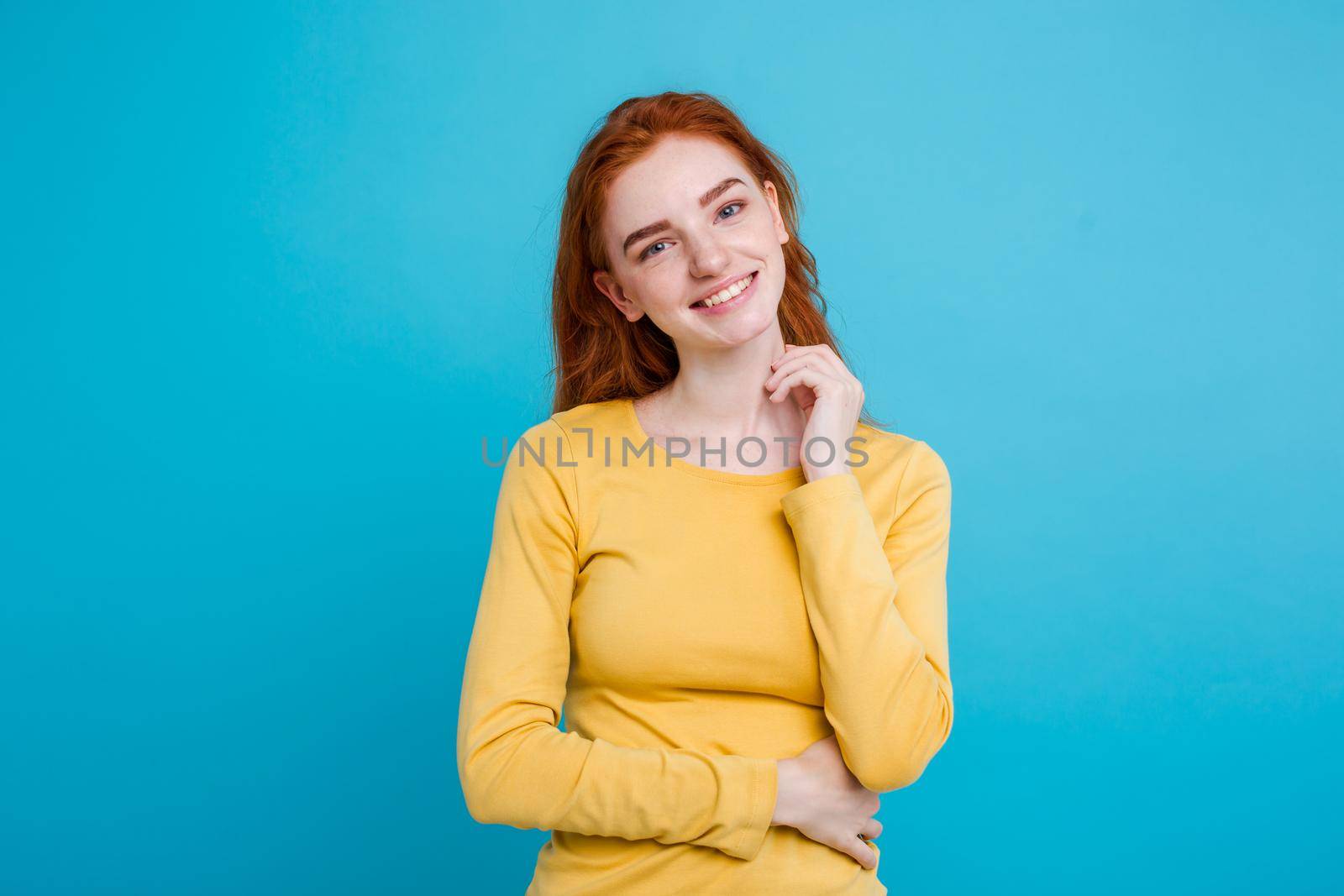 Portrait of happy ginger red hair girl with freckles smiling looking at camera. Pastel blue background. Copy Space by Benzoix