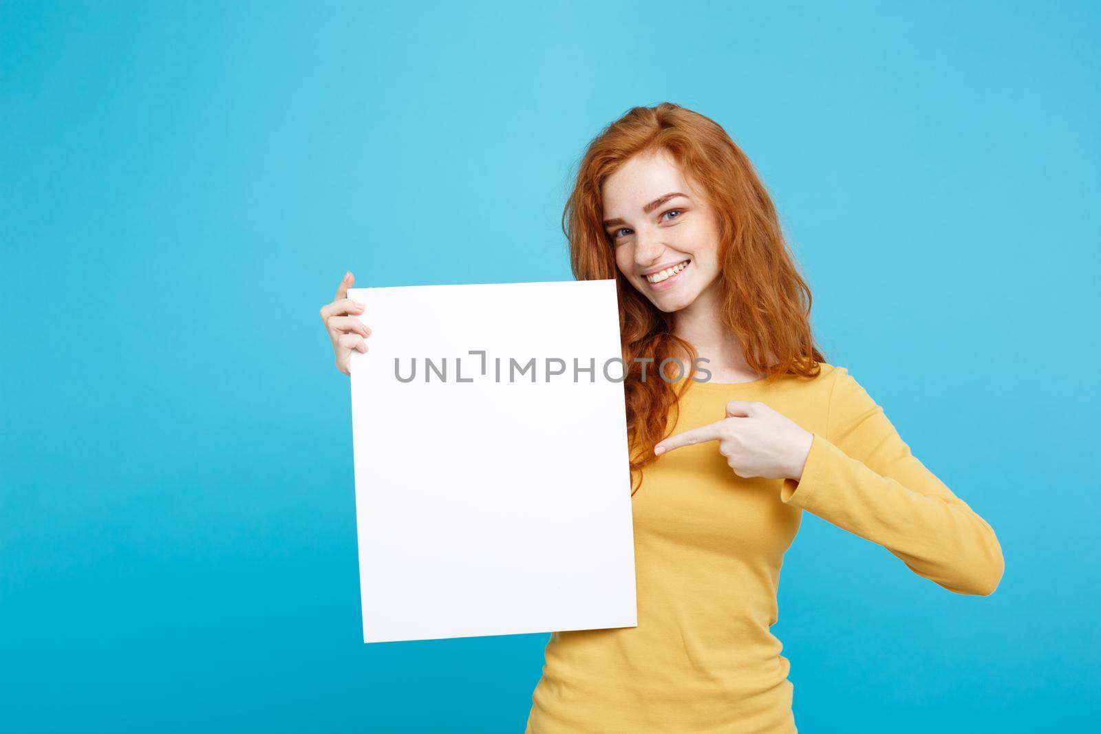 Close up Portrait young beautiful attractive ginger red hair girl smiling showing blank sign. Blue Pastel Background. Copy space. by Benzoix