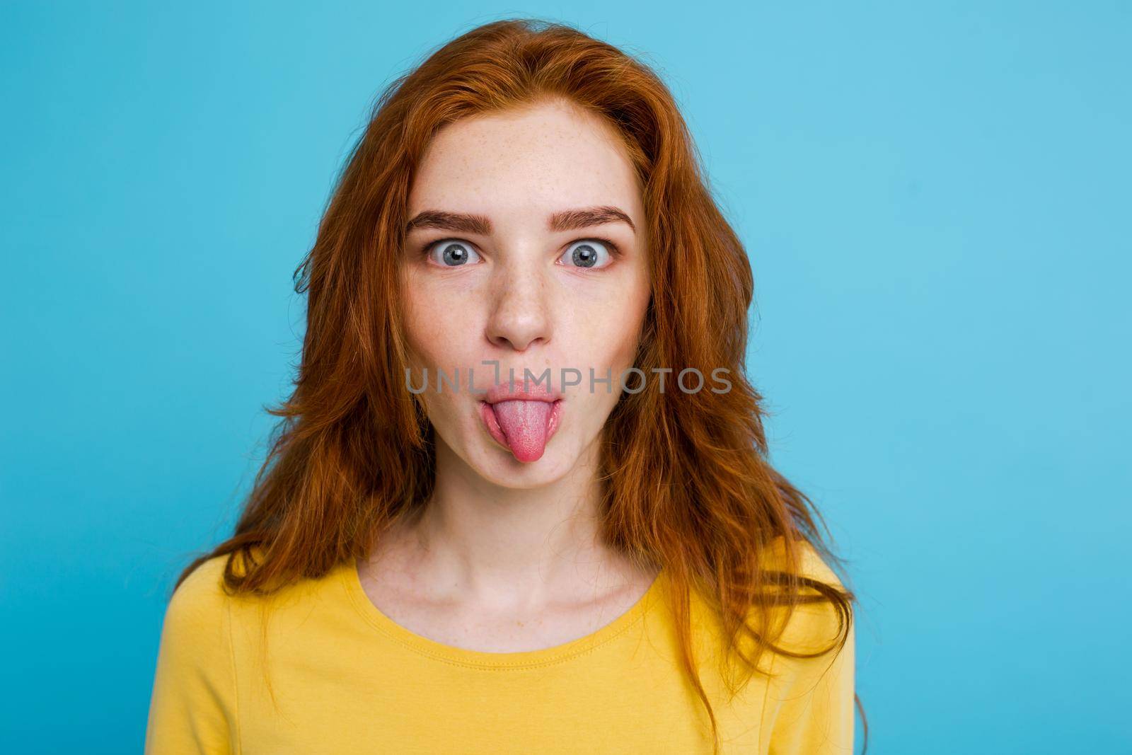 Headshot Portrait of happy ginger red hair girl with funny face looking at camera. Pastel blue background. Copy Space.