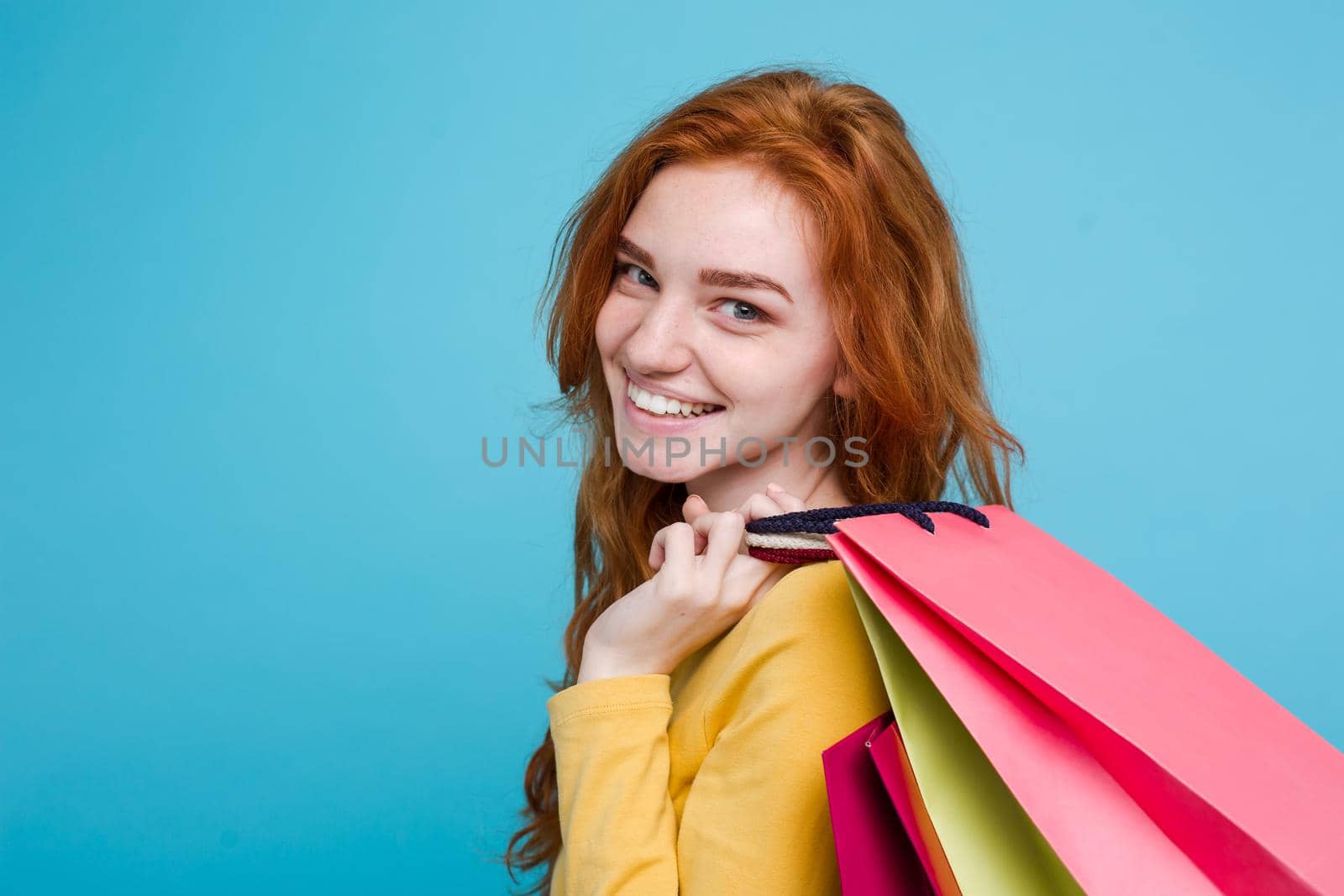 Shopping Concept - Close up Portrait young beautiful attractive redhair girl smiling looking at camera with shopping bag. Blue Pastel Background. Copy space by Benzoix