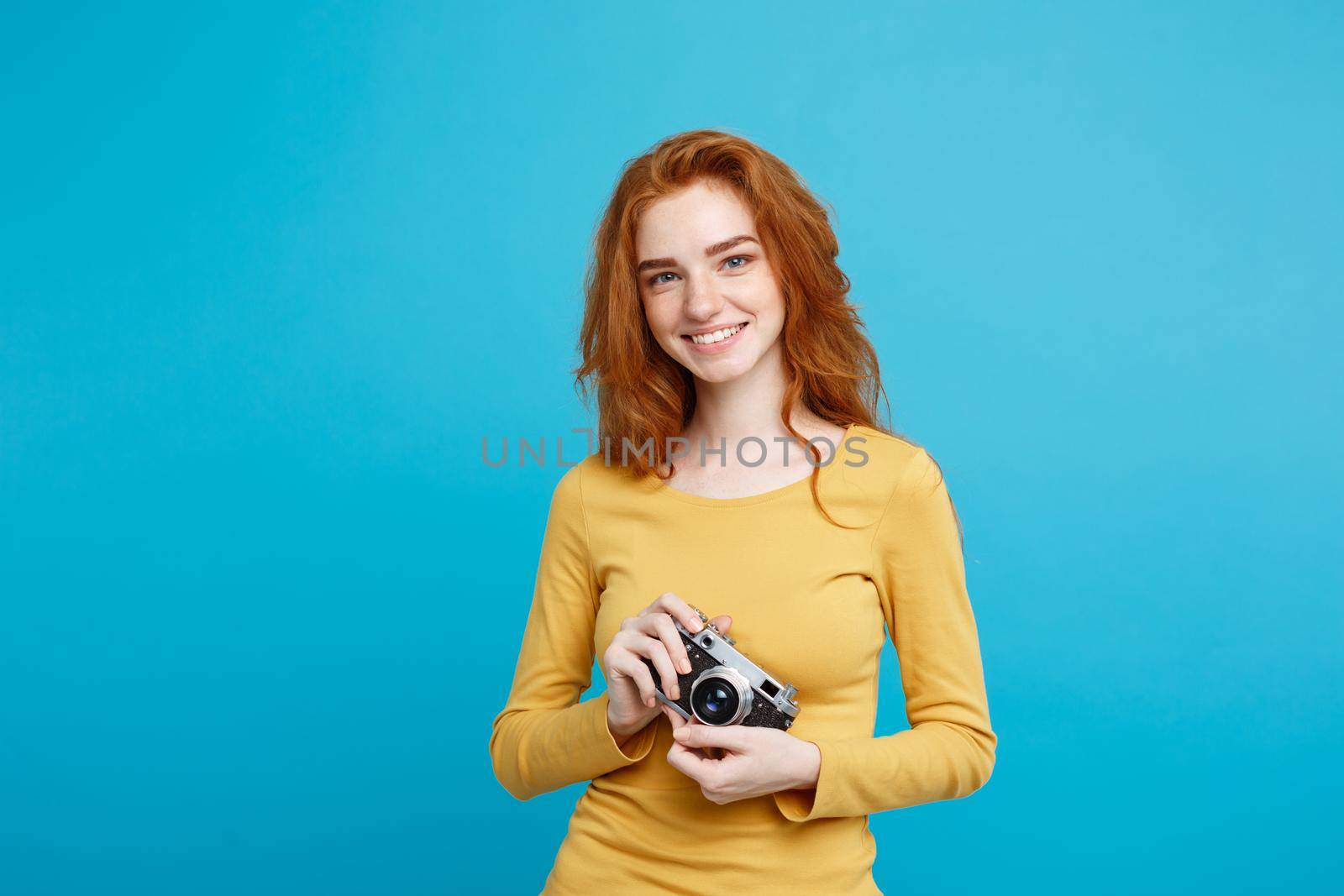 Close up Portrait young beautiful attractive ginger girl happy smiling with vintage camera and ready to travel. Isolated on Blue Pastel Background. Copy space. by Benzoix