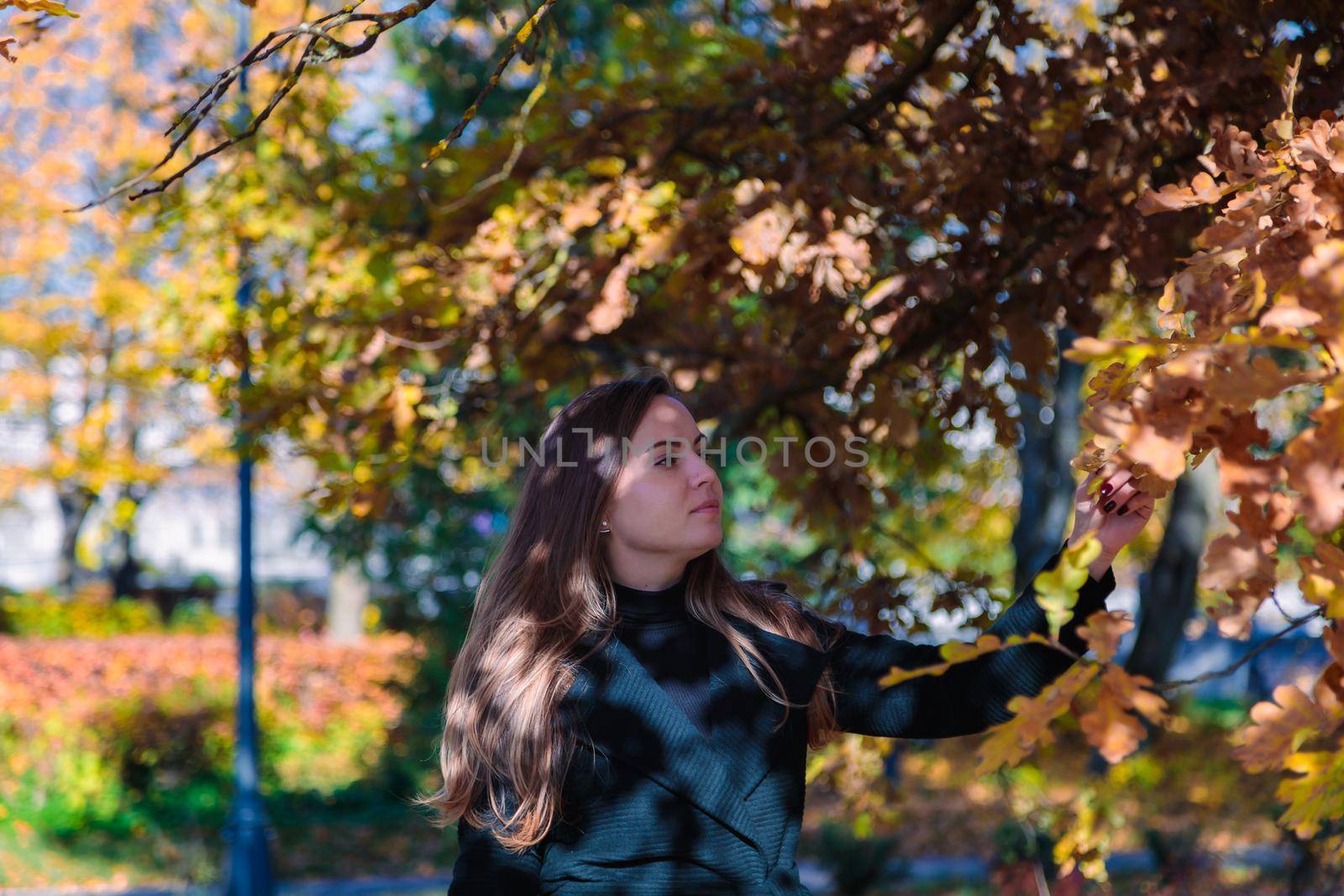 A woman with long hair looks at yellow leaves in an autumn park. Autumn season.