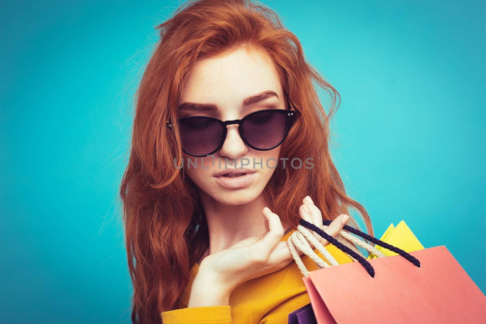 Shopping Concept - Close up Portrait young beautiful attractive redhair girl smiling looking at camera with shopping bag. Blue Pastel Background. Copy space.