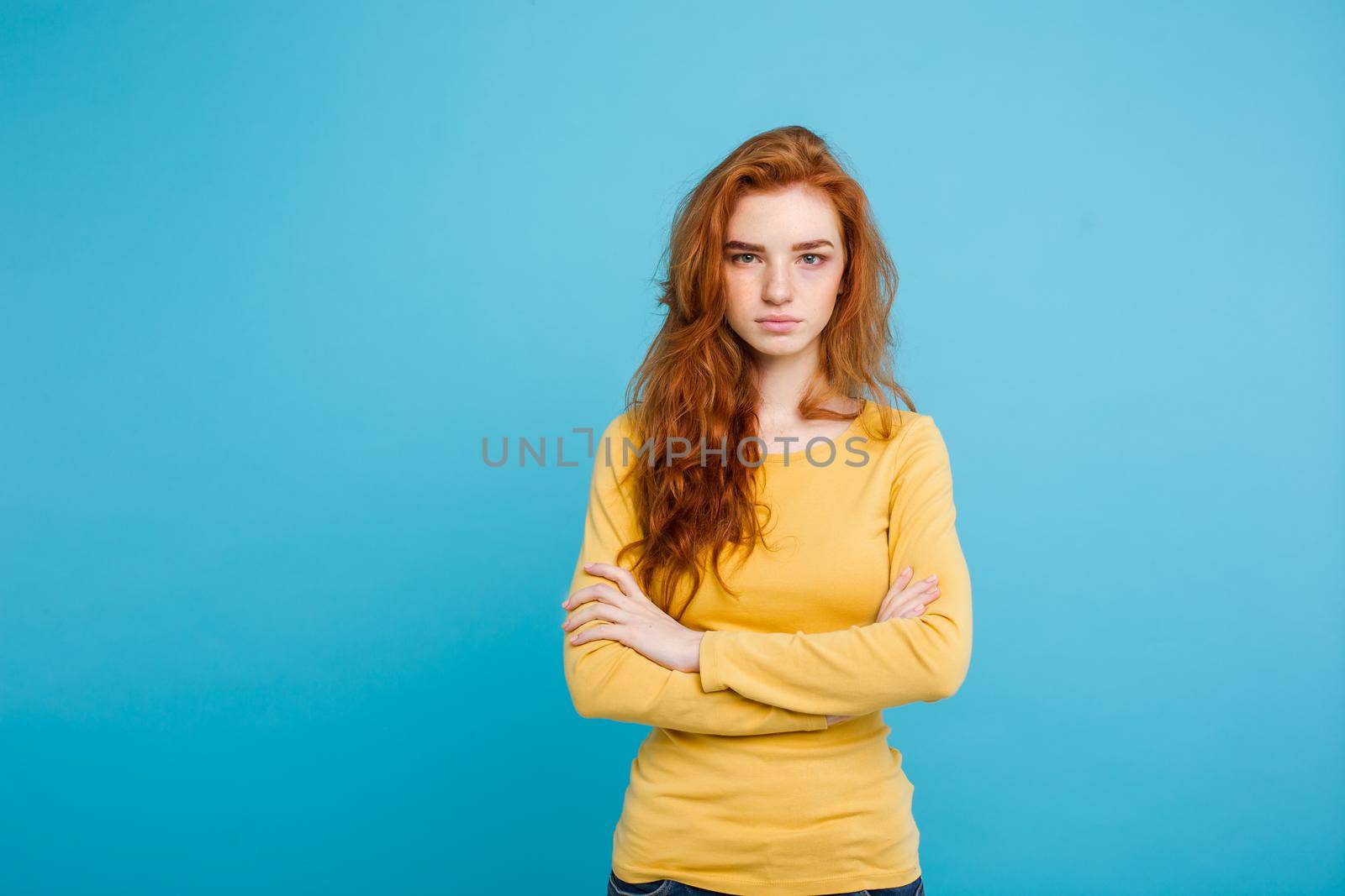 Portrait of young beautiful ginger woman with tender serious face crossing arms looking at camera. Isolated on pastel blue background. Copy space by Benzoix