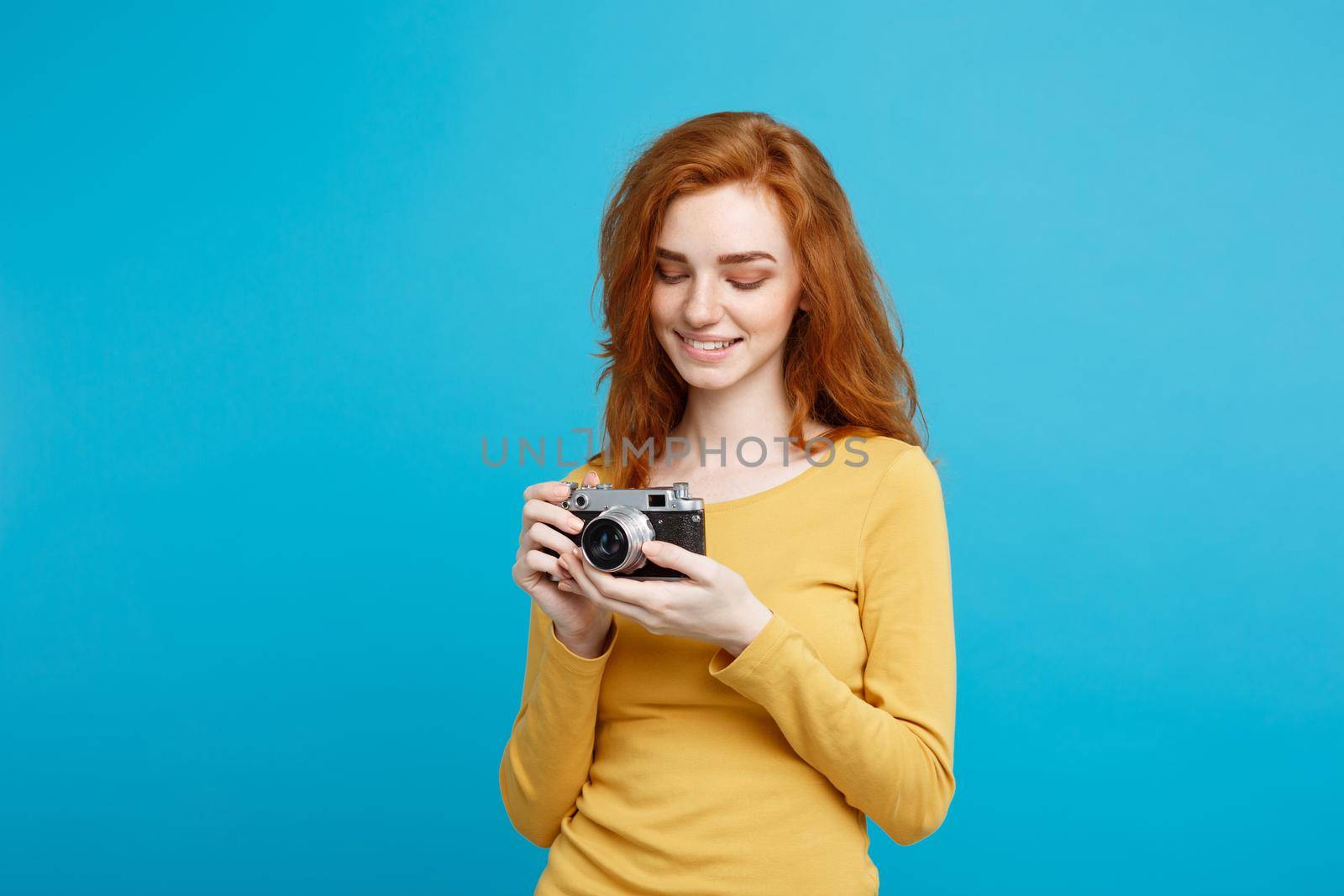 Travel and People Concept - Headshot Portrait of happy ginger red hair girl with playing with vintage camera in happy expression. Pastel blue background. Copy Space.