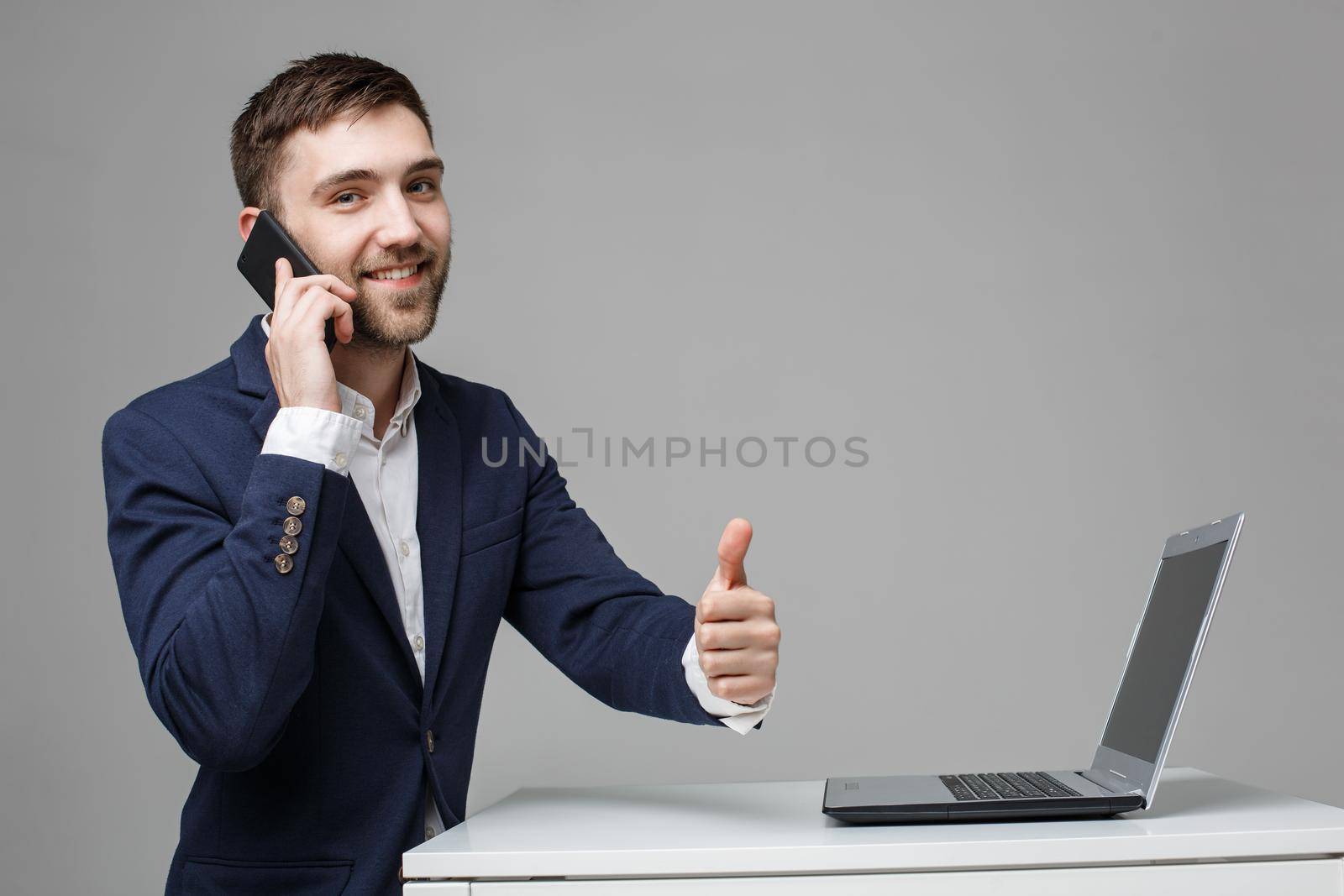 Businessman showing thumbs up while using laptop in office by Benzoix