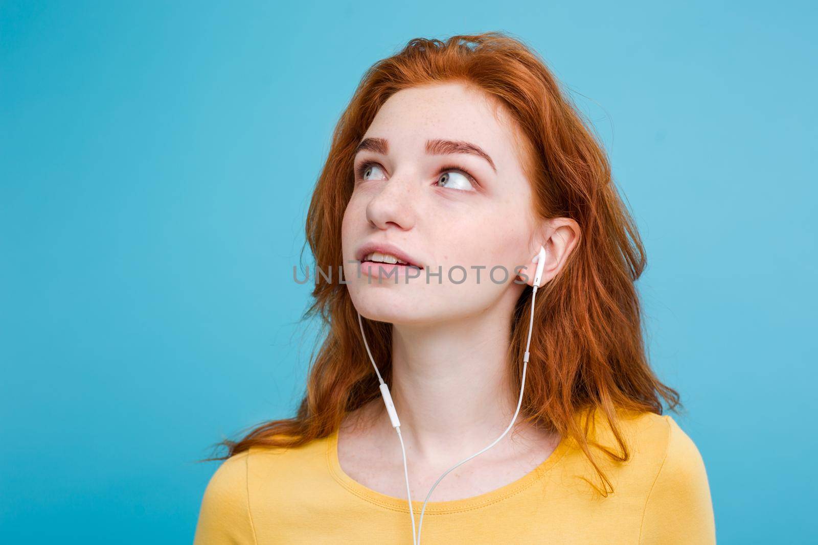 Lifestyle concept - Portrait of cheerful happy ginger red hair girl enjoy listening to music with headphones joyful smiling to camera. Isolated on Blue Pastel Background. Copy space by Benzoix