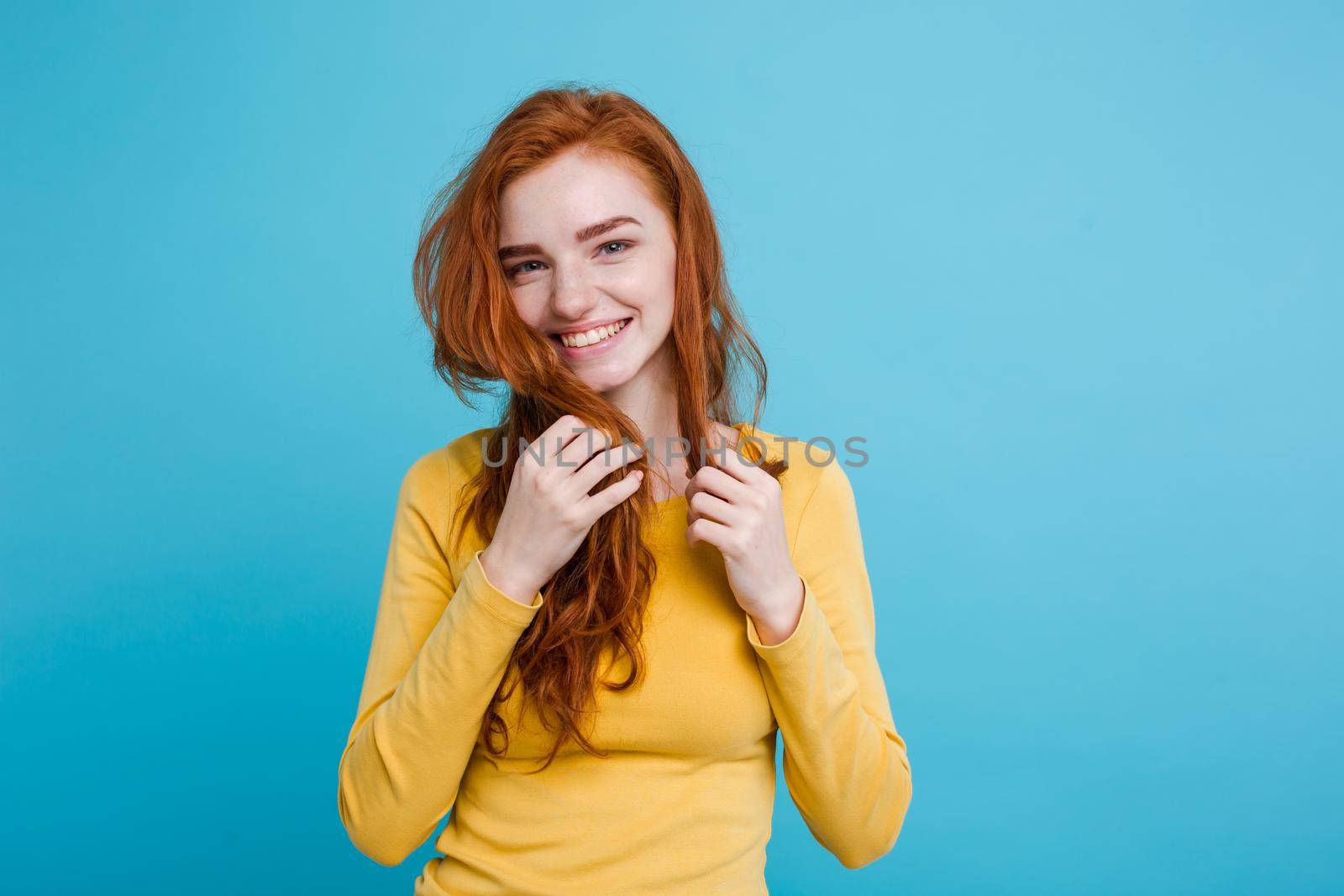 Portrait of happy ginger red hair girl with freckles smiling looking at camera. Pastel blue background. Copy Space.