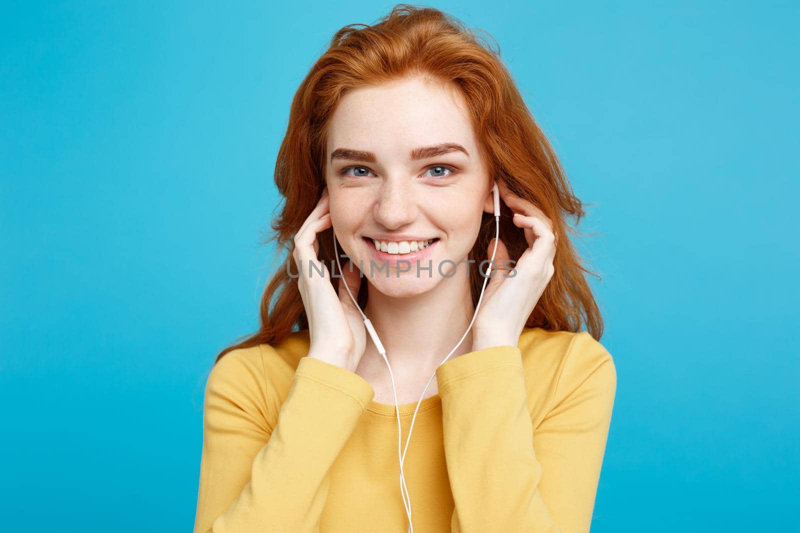 Lifestyle concept - Portrait of cheerful happy ginger red hair girl enjoy listening to music with headphones joyful smiling to camera. Isolated on Blue Pastel Background. Copy space.