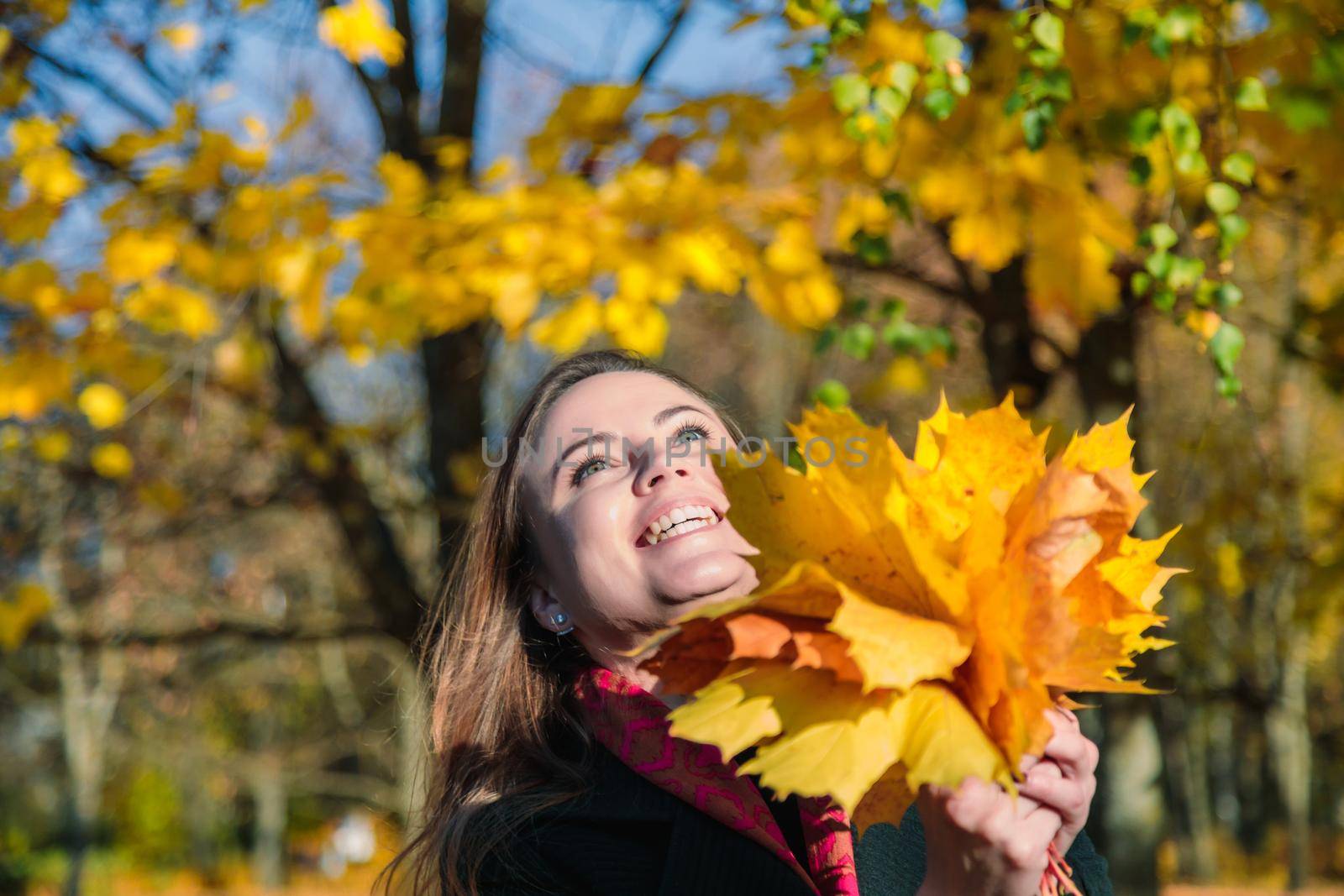 A woman with long hair rejoices at a yellow bouquet of leaves in an autumn park. by Yurich32