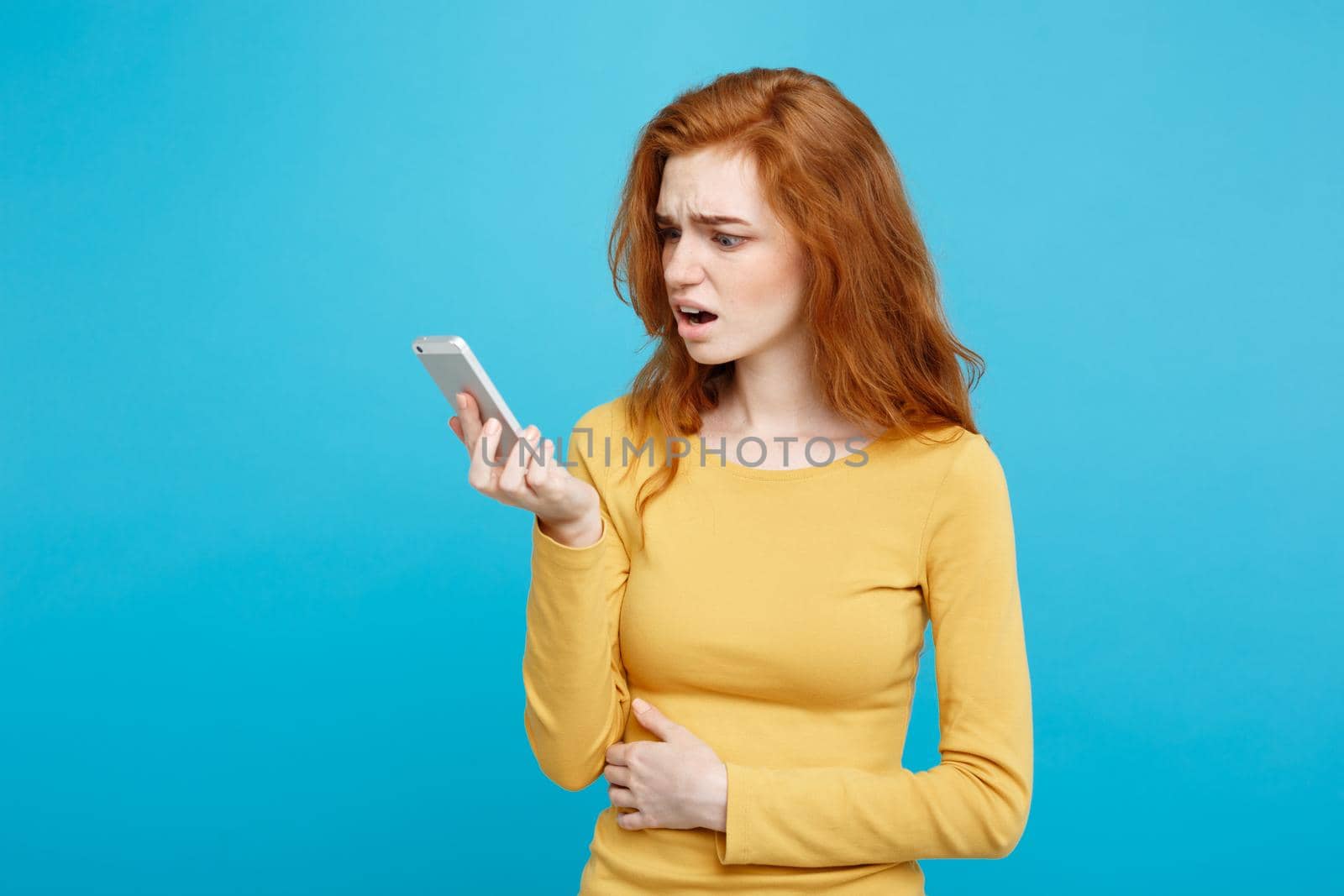 Lifestyle concept - Portrait of a shocked surprised girl in yellow dress talking on mobile phone. Isolated on Blue Pastel Background. Copy space.
