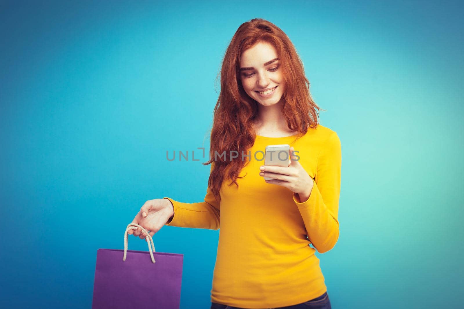 Shopping Concept - Close up Portrait young beautiful attractive redhair girl smiling looking at camera with shopping bag. Blue Pastel Background. Copy space by Benzoix