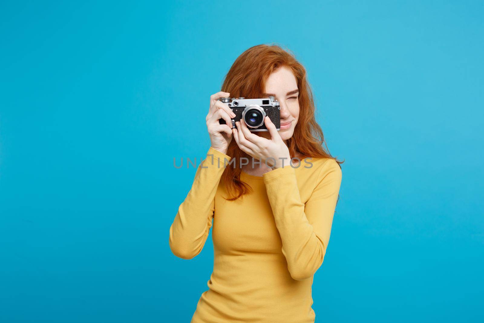 Travel and People Concept - Headshot Portrait of happy ginger red hair girl with playing with vintage camera in happy expression. Pastel blue background. Copy Space.
