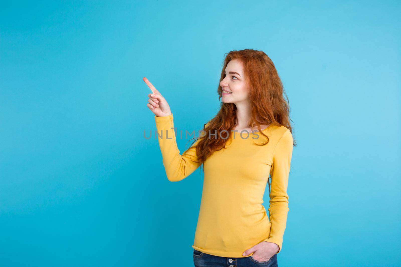 Close up Portrait young beautiful attractive redhair girl happy with something and pointing finger. Blue Pastel Background. Copy space.